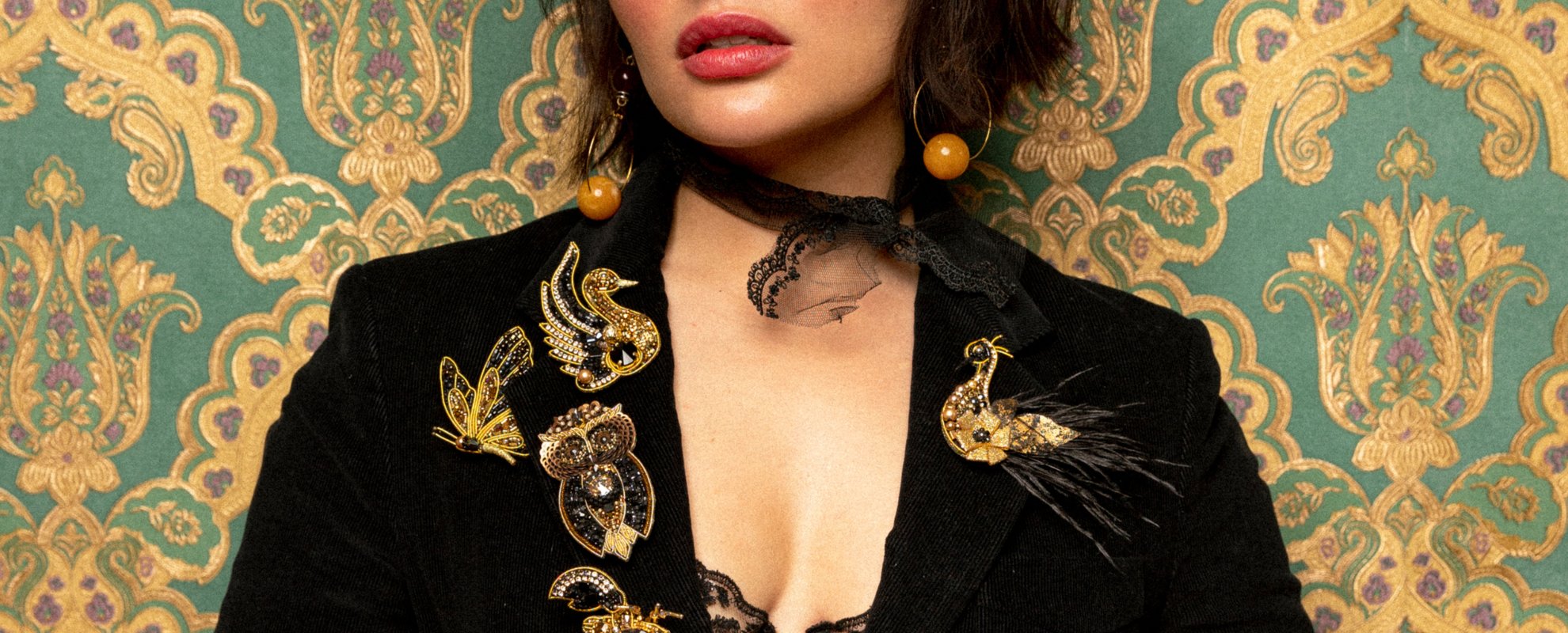 Girl wearing a purple top and she has a beaded bird brooch and beaded dragonfly brooch pinned to her 