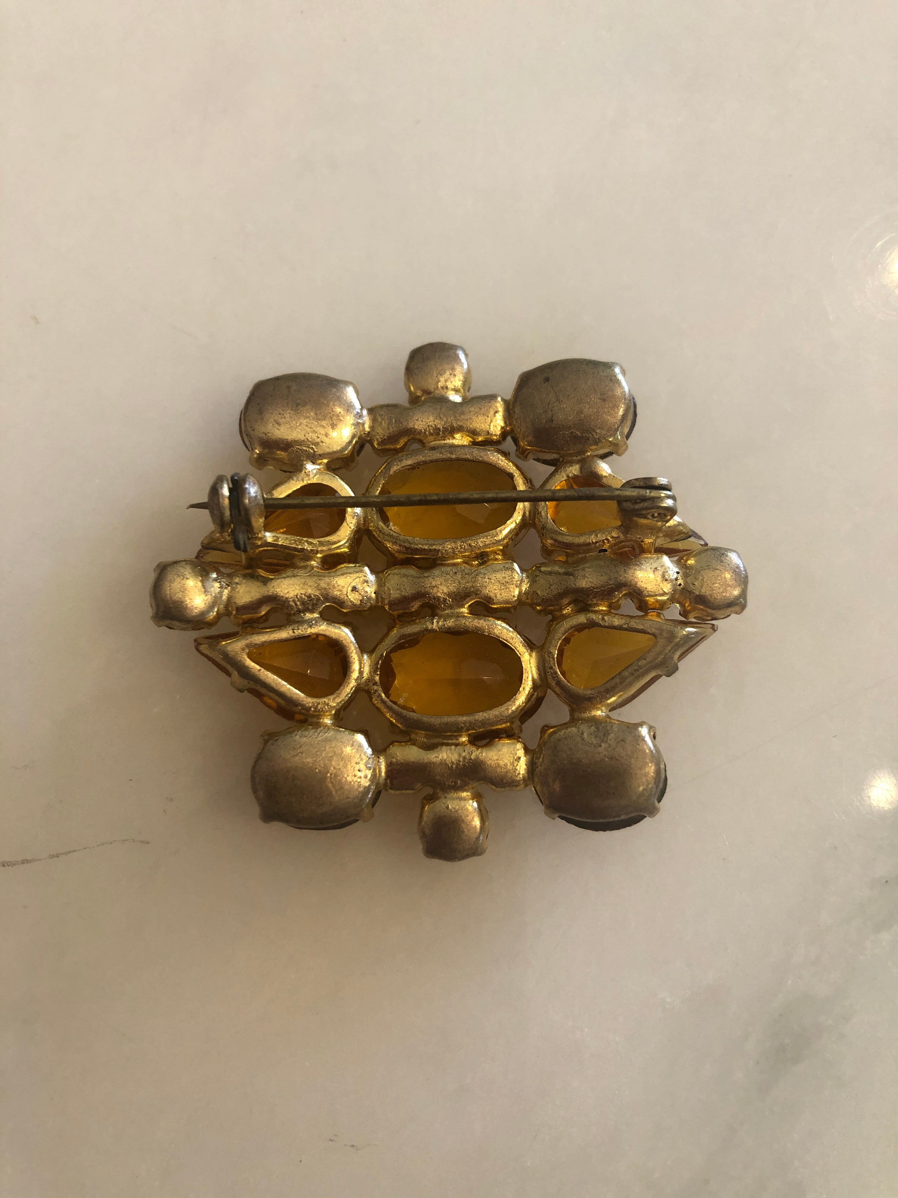 A 4.5cm x 4.5cm vintage gold-tone cluster brooch featuring large faceted oval and pear-cut amber crystal stones with graduating round amber rhinestone accents in a layered sculptural arrangement, photographed on marble table