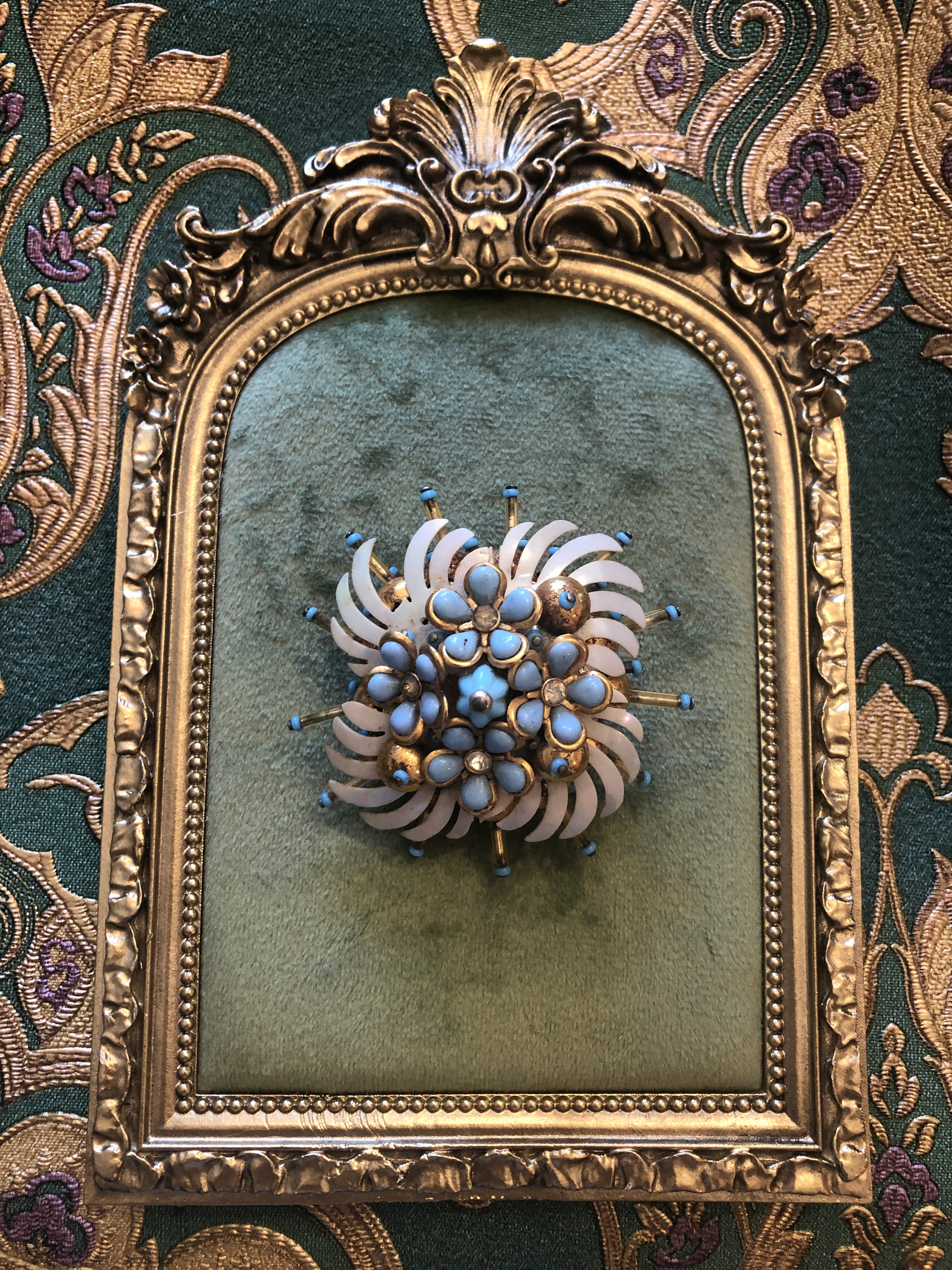 A 6cm x 6cm vintage gold-tone floral burst brooch featuring layered white enamel swept petals, a dense centre cluster of powder blue cabochon flowers set in gold-tone bezels with crystal rhinestone accents, and radiating spike pins tipped in powder blue.