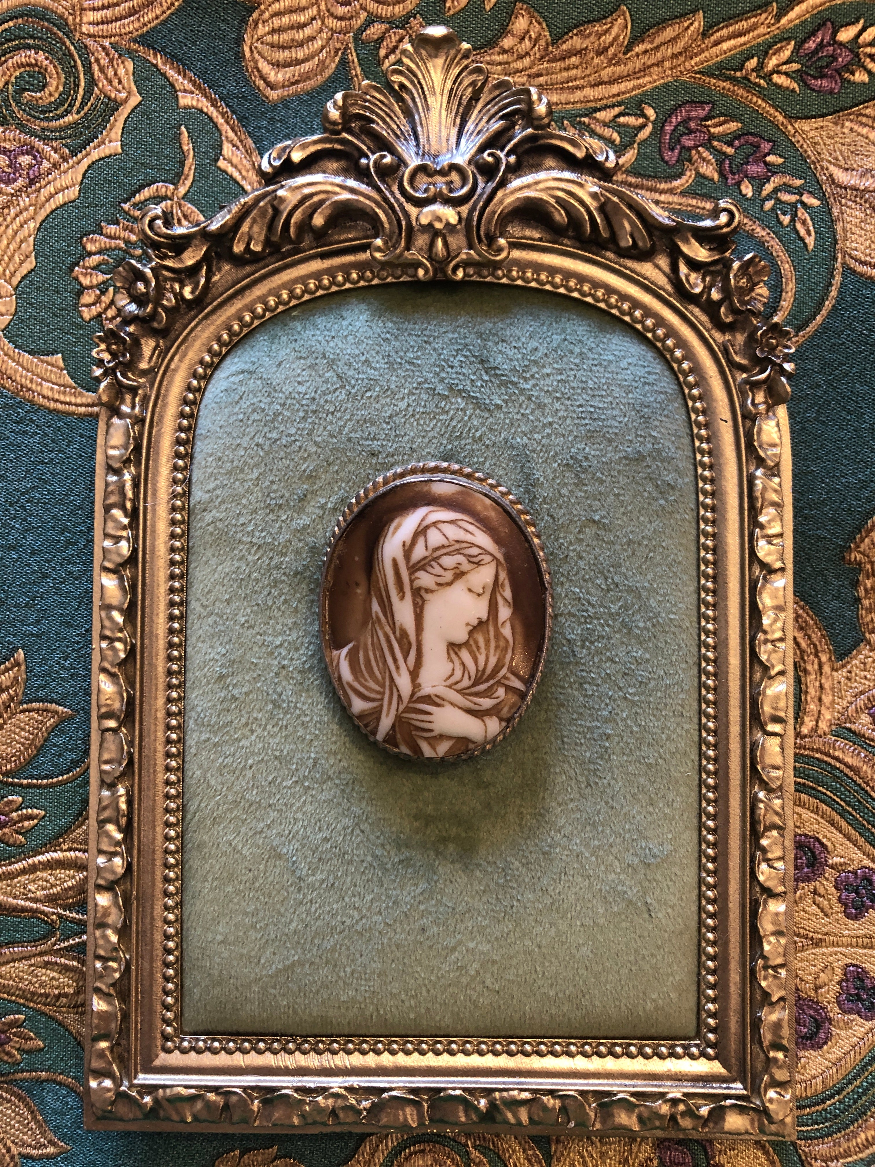  5cm x 4cm vintage signed Cordia cameo brooch with a carved white relief Madonna portrait with bowed head and clasped hands on a warm brown ground, in a silver-tone twisted rope frame, photographed on a white marble surface.