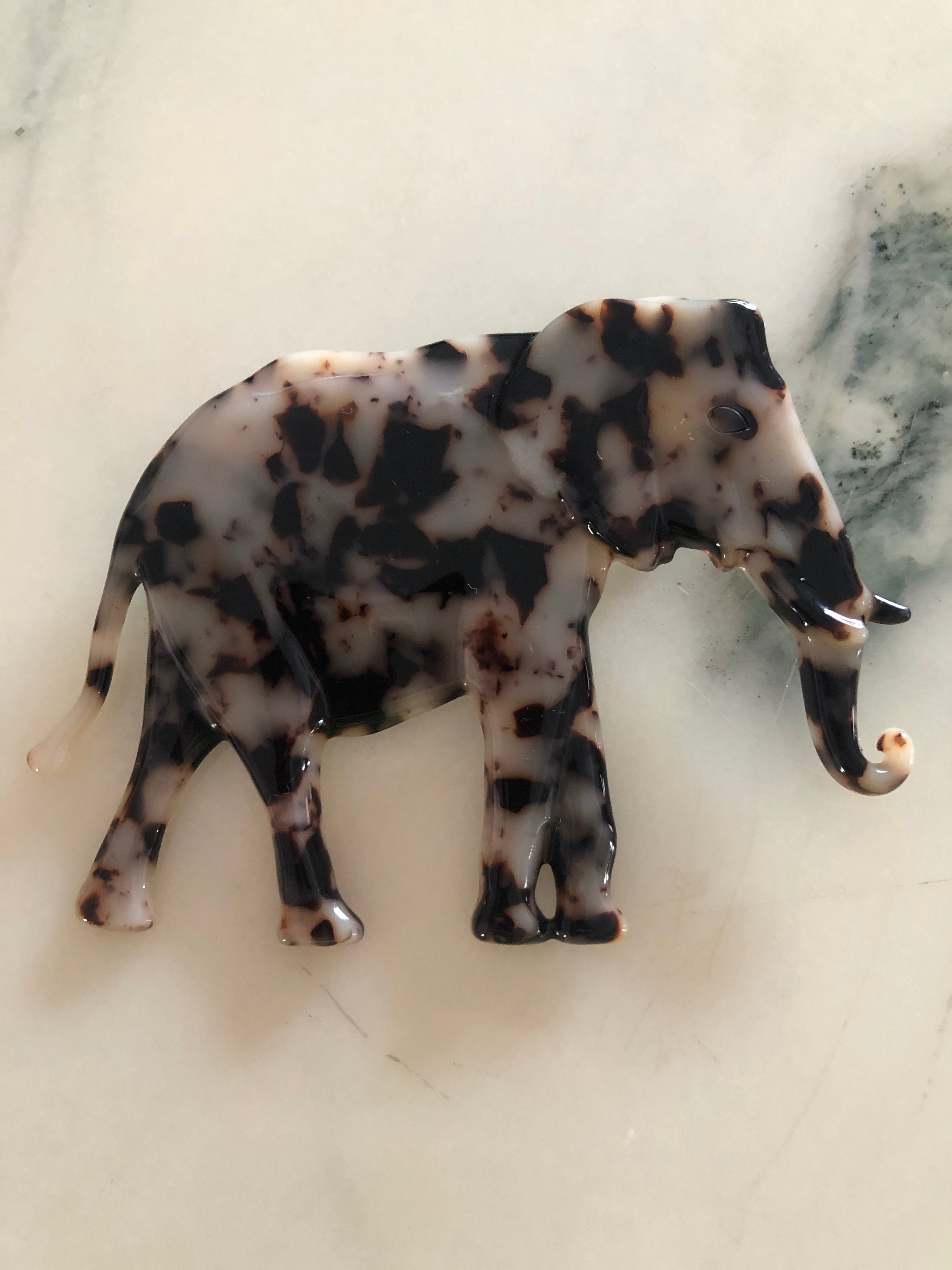 Men's elephant brooch in brown tortoiseshell acetate. Pictured on a white marble background