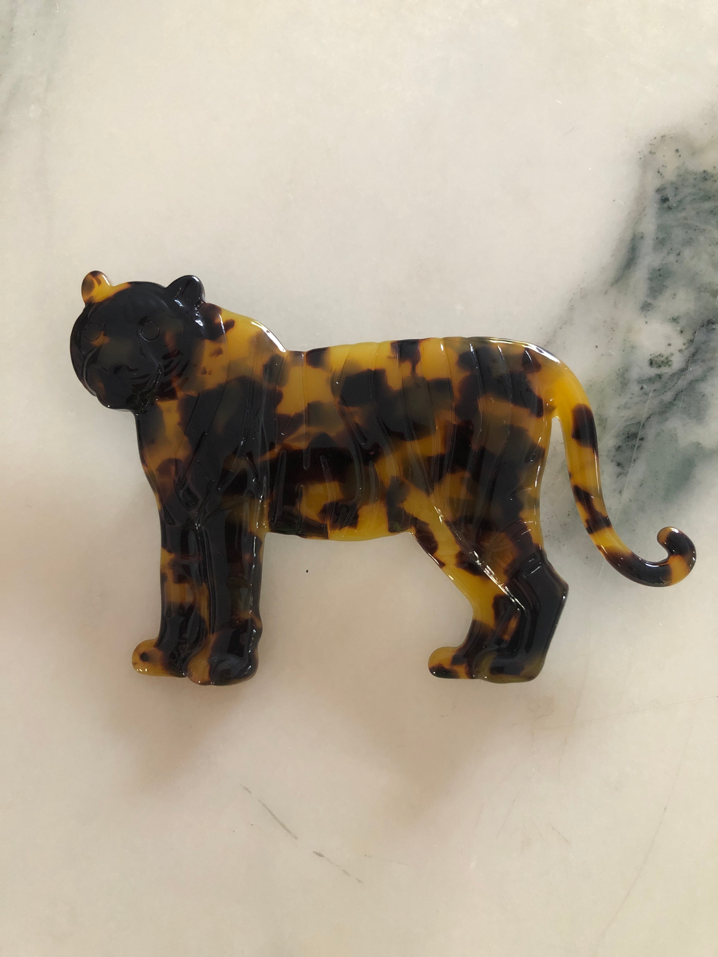 Men's tiger brooch in brown tortoiseshell acetate. The background is white marble