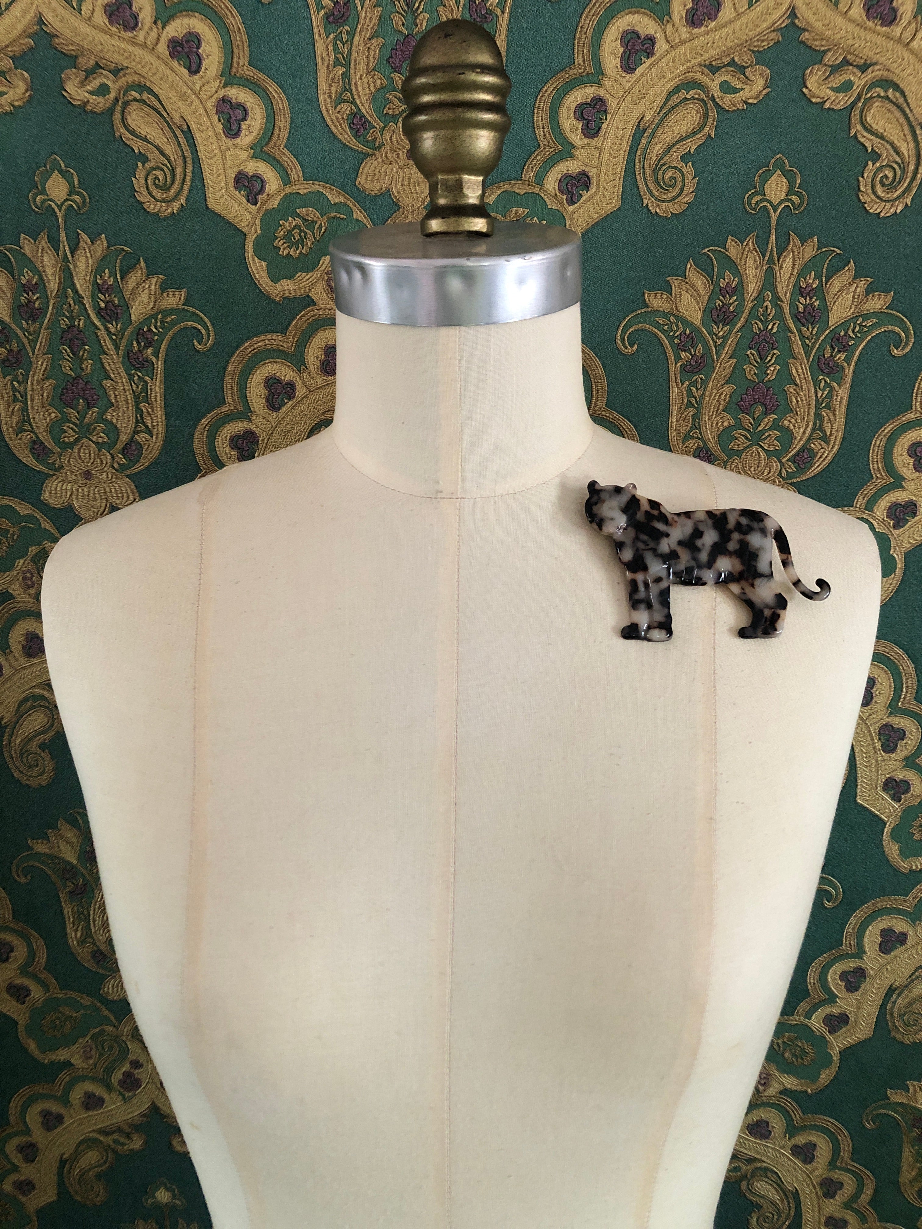 A Broochella Animalia Collection tiger brooch in black and white tortoiseshell Italian cellulose acetate with natural spot patterning measuring 7cm x 10cm, photographed on a white marble surface.