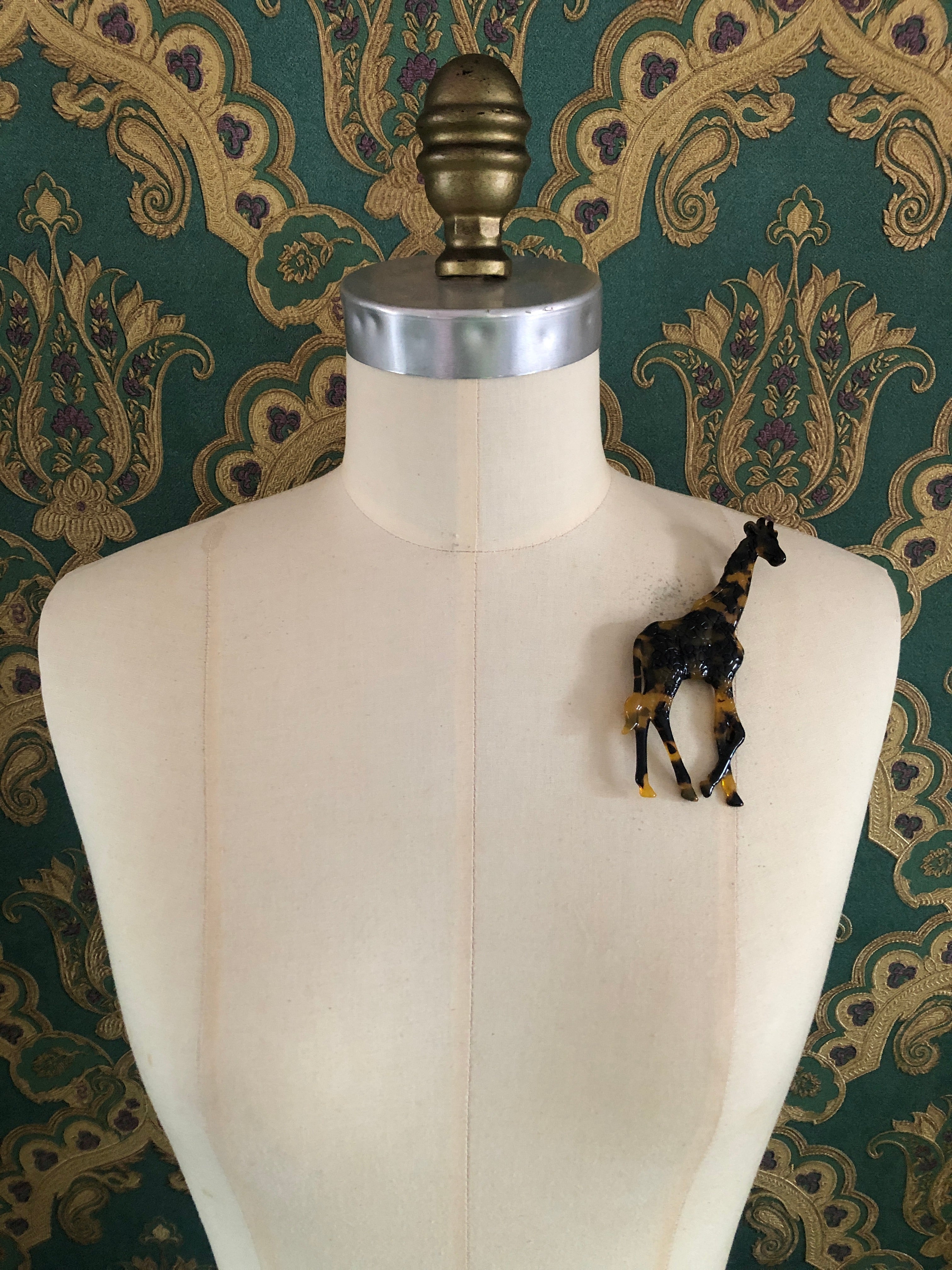 A Broochella Animalia Collection standing giraffe brooch in black and white tortoiseshell Italian cellulose acetate with sculpted spot patterning measuring 12cm x 7cm, photographed on a white marble surface.