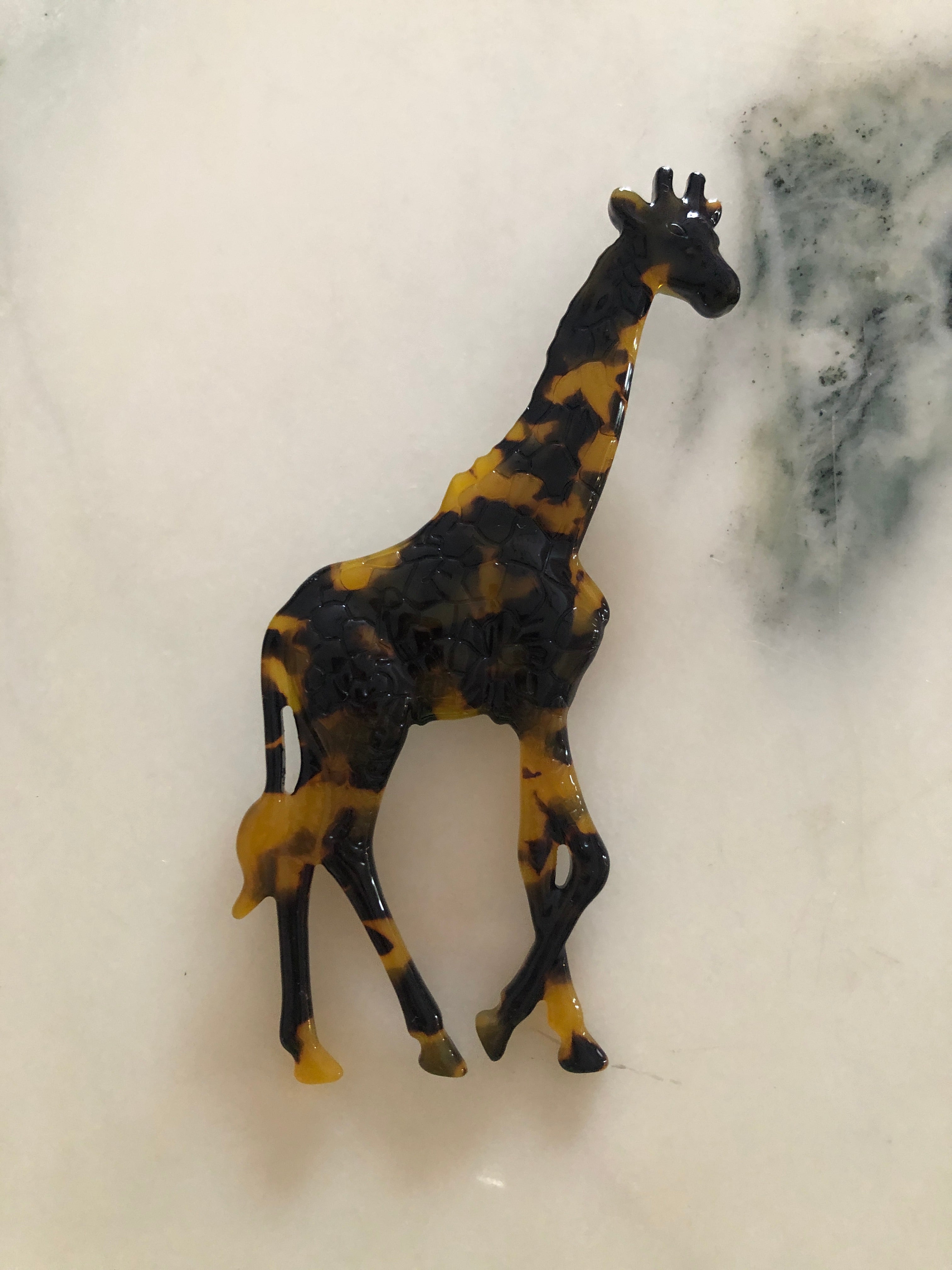 A Broochella Animalia Collection standing giraffe brooch in black and white tortoiseshell Italian cellulose acetate with sculpted spot patterning measuring 12cm x 7cm, photographed on a white marble surface.