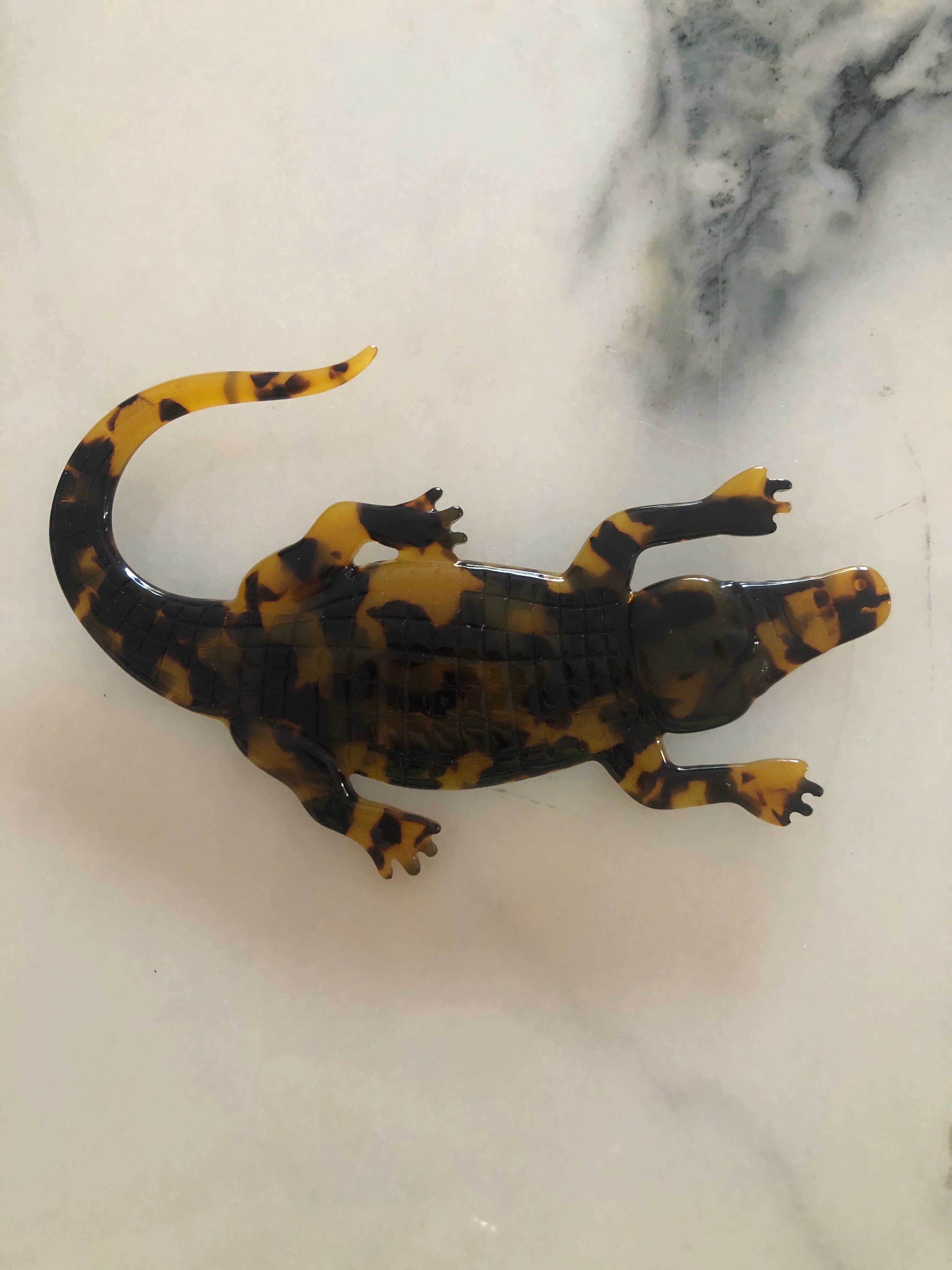 Men's alligator brooch in brown tortoiseshell acetate. The bacground is white marble