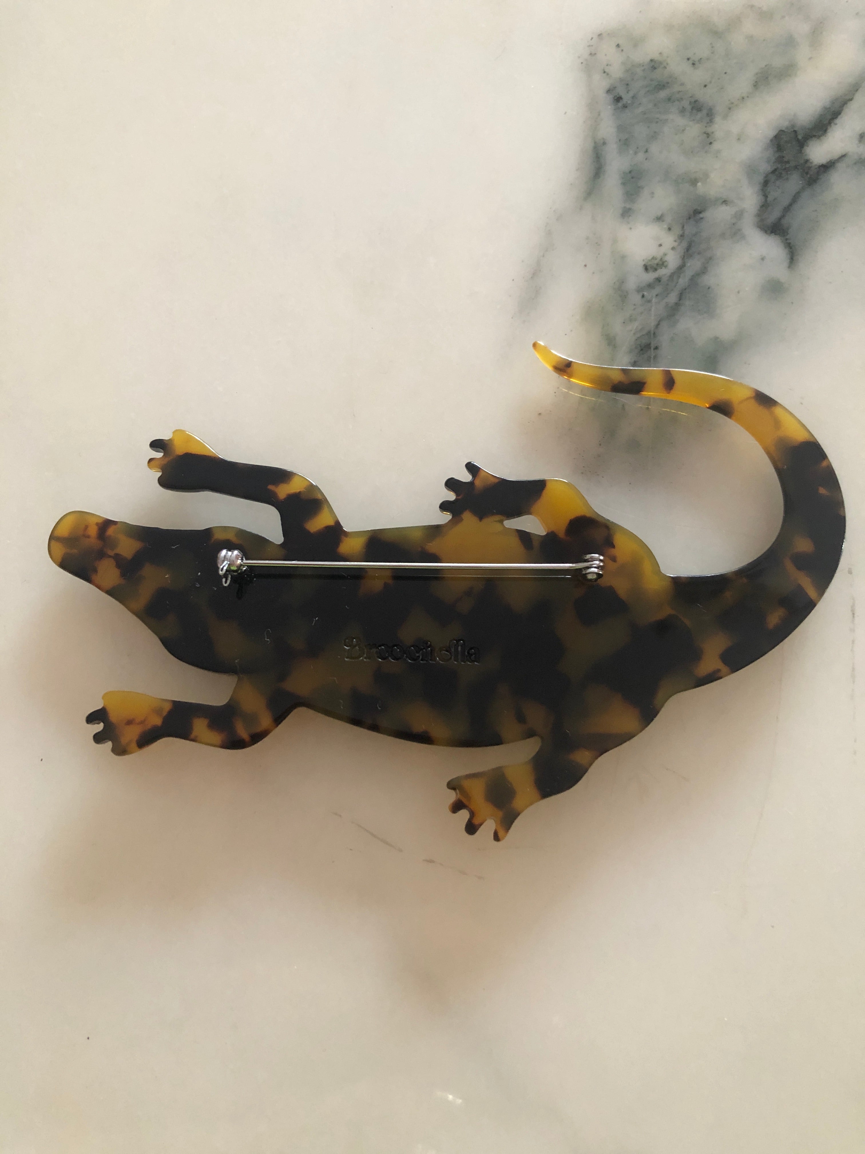 A Broochella Animalia Collection alligator brooch in brown tortoiseshell Italian cellulose acetate with detailed scale texture measuring 7cm x 12cm, photographed on a white marble surface.