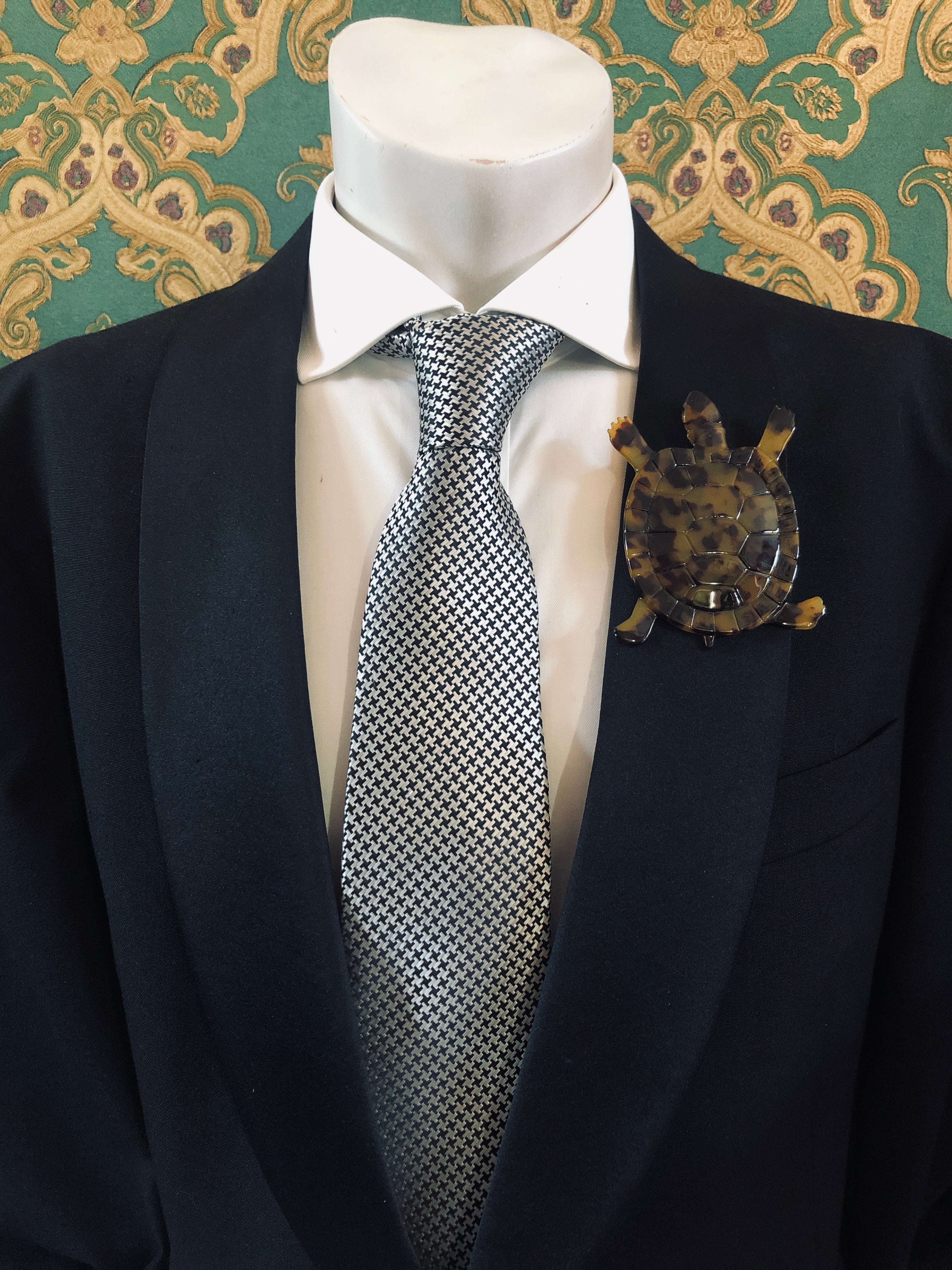 Men's tortoise brooch in brown tortoiseshell acetate worn on a black tailored jacket with silver houndstooth tie, from the Broochella Animalia Collection.