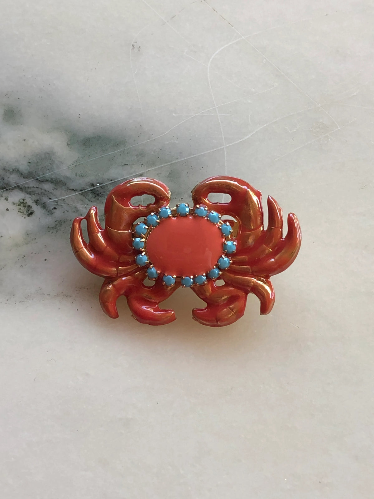 Broochella Sacro Cuore Granchio Crab Brooch in glossy coral enamel with turquoise stones and gold detailing, photographed on a white marble background.