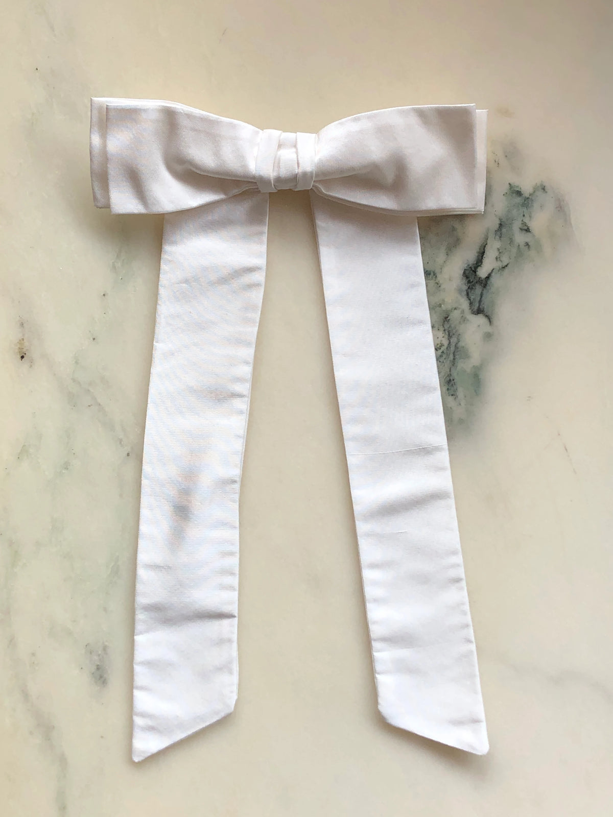 Handmade Broochella Alice Silk Bow Brooch in elegant ivory dupion silk, featuring an oversized designer bow with long elegant tails and a lustrous natural silk texture, photographed on white marble.
