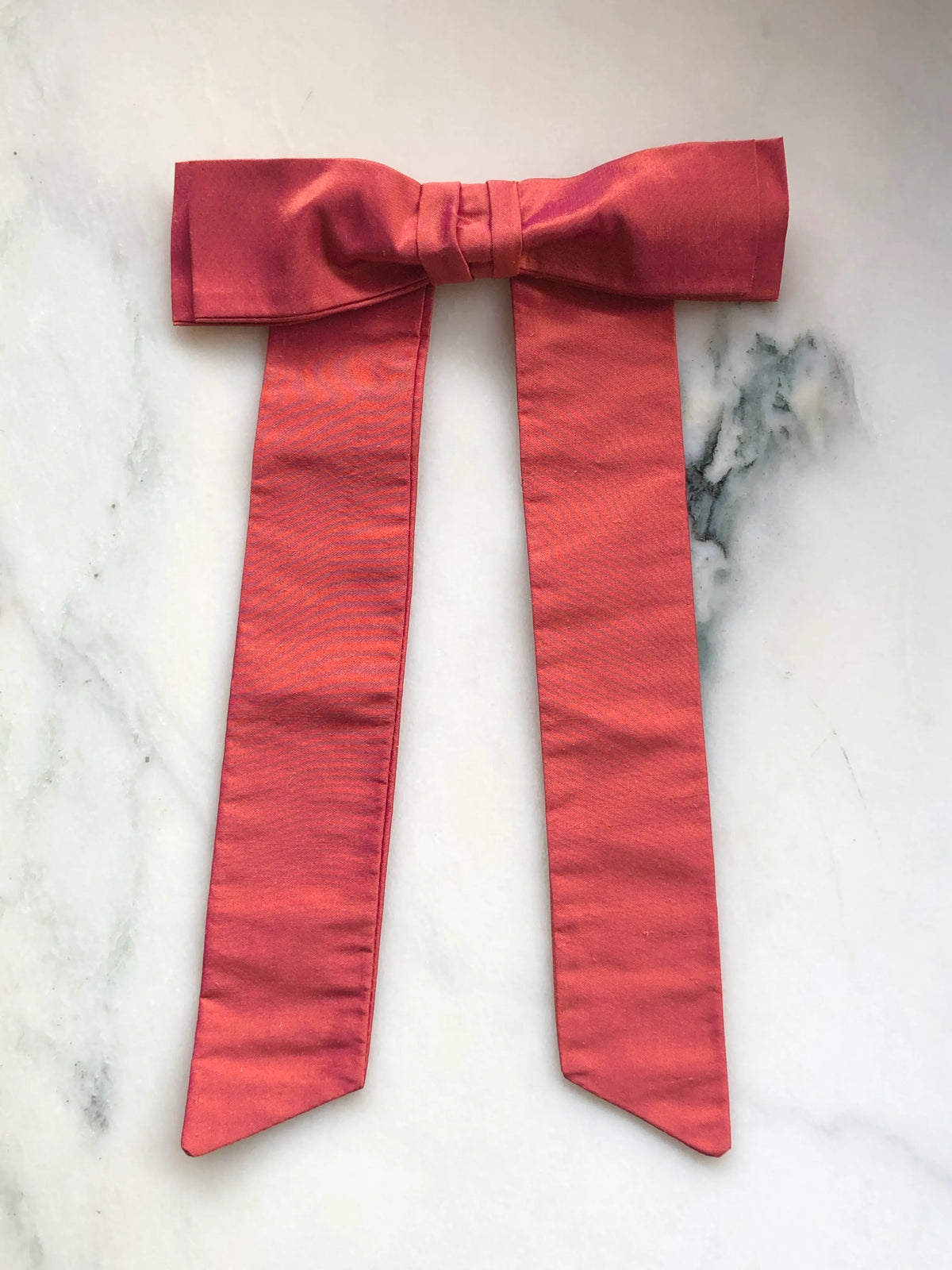 Handmade Broochella Men’s Alice Silk Bow Brooch in warm peach dupion silk, featuring an oversized designer bow with long tailored tails and a lustrous natural silk texture, photographed on white marble.