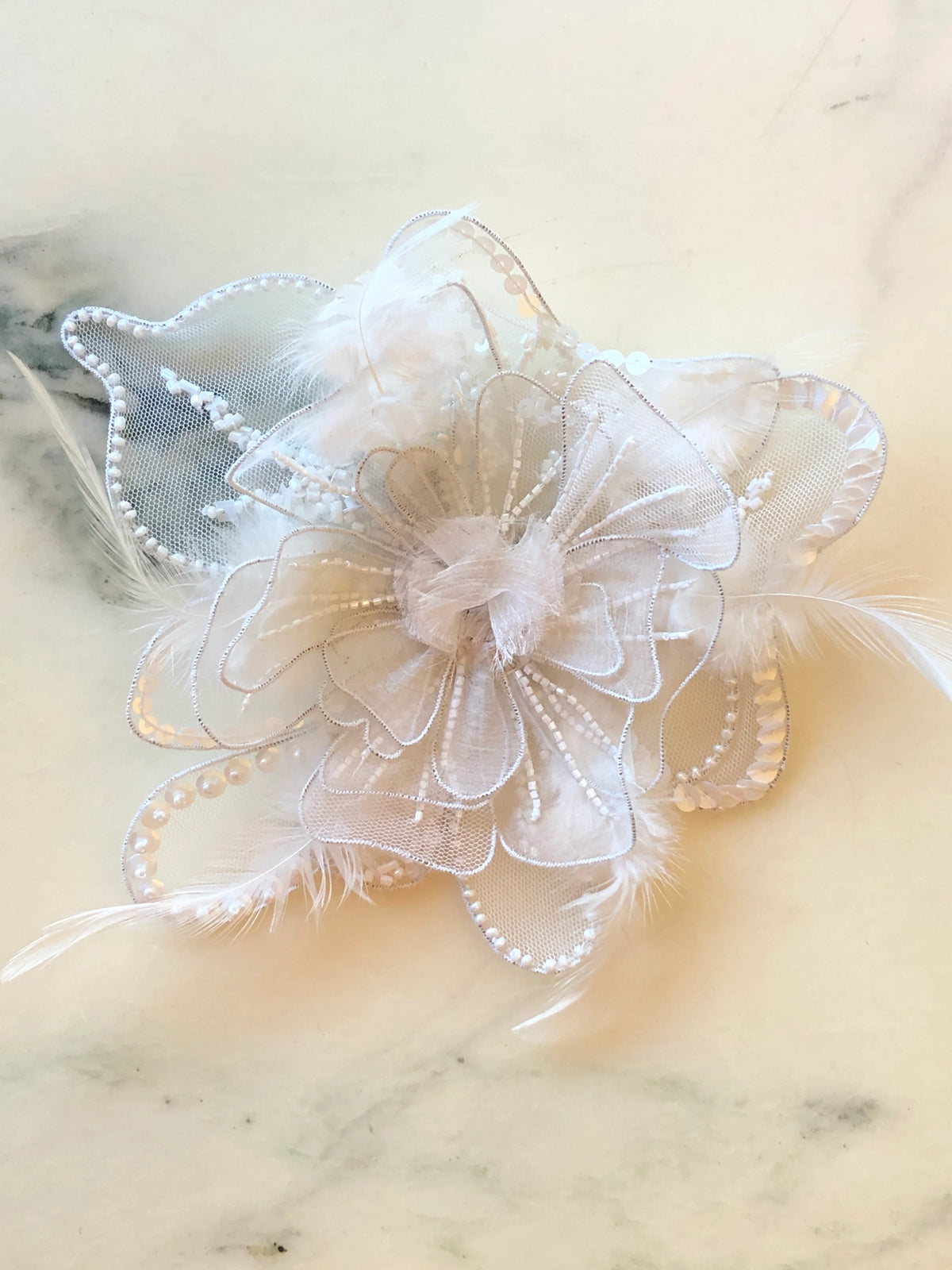 Broochella Alstroemeria Hand-Beaded Flower Brooch - Small in white, featuring layered sheer organza petals embellished with white beads, sequins and delicate feather accents on a cream marble background.