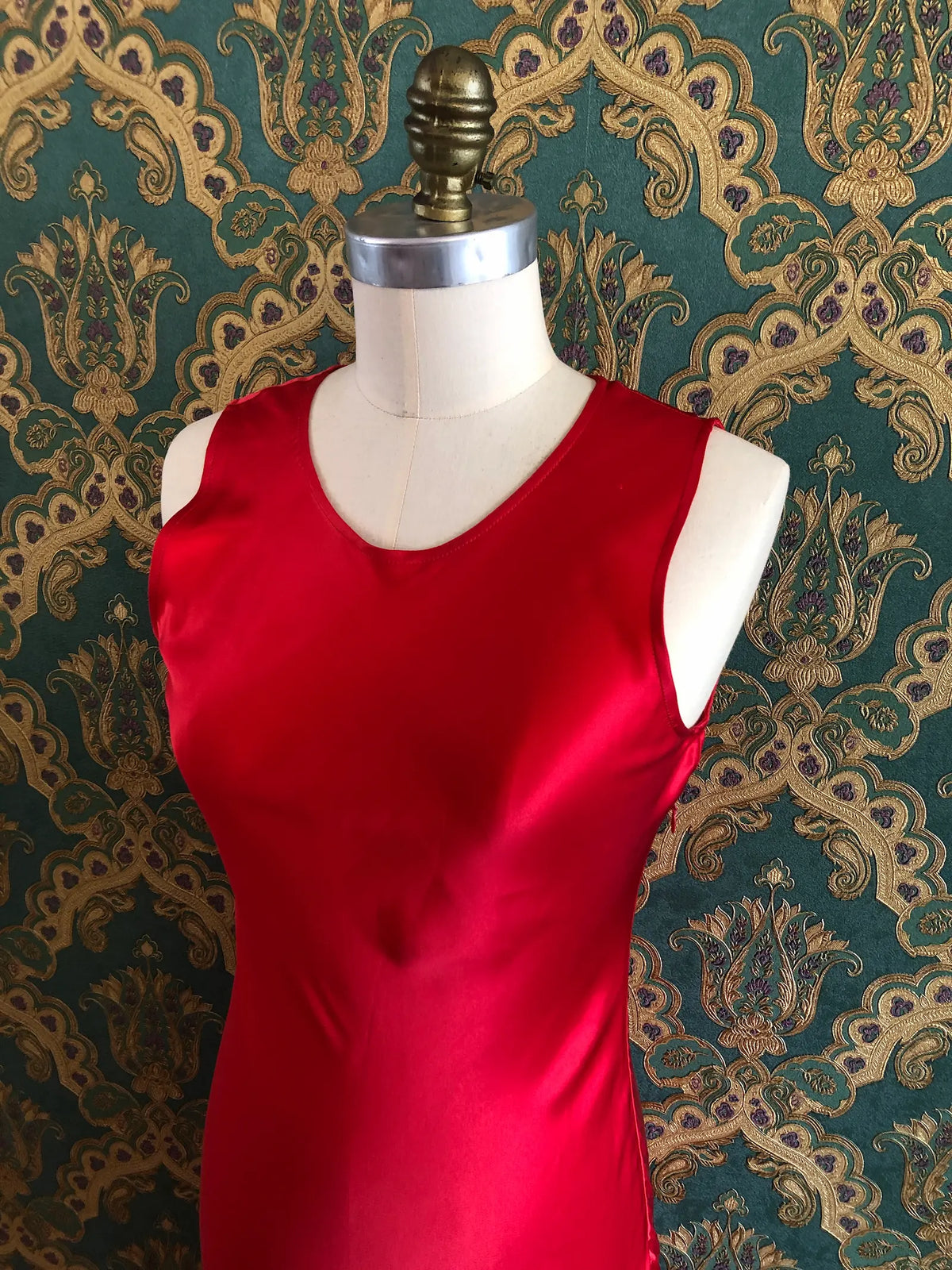 Broochella Amāre scarlet red silk maxi dress with a round neckline, sleeveless bodice and dramatic long panelled fringe, size AU 10. Pictured on a mannequin against green and gold damask wallpaper.