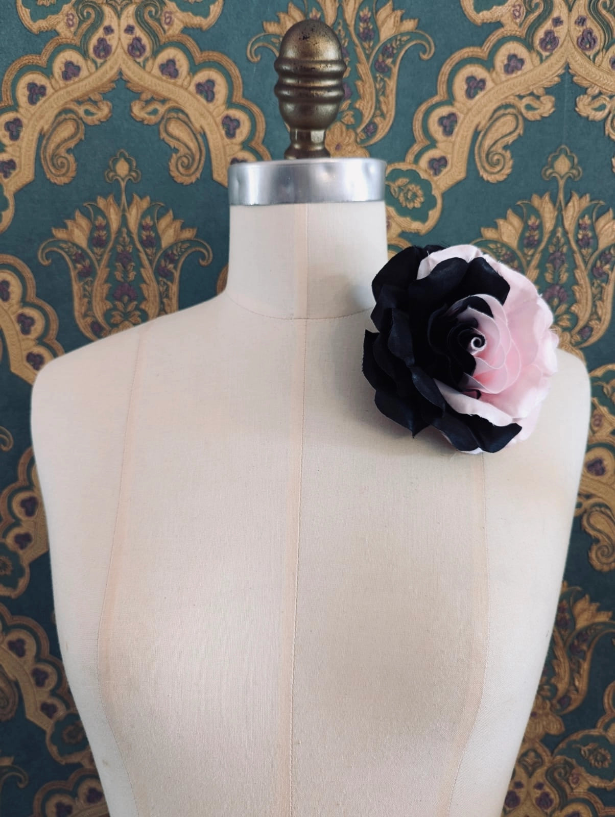 Broochella amore nella notte handmade fabric flower brooch in half pink and half black. The brooch is pinned to a mannequin. The background is green and gold damask wallpaper.