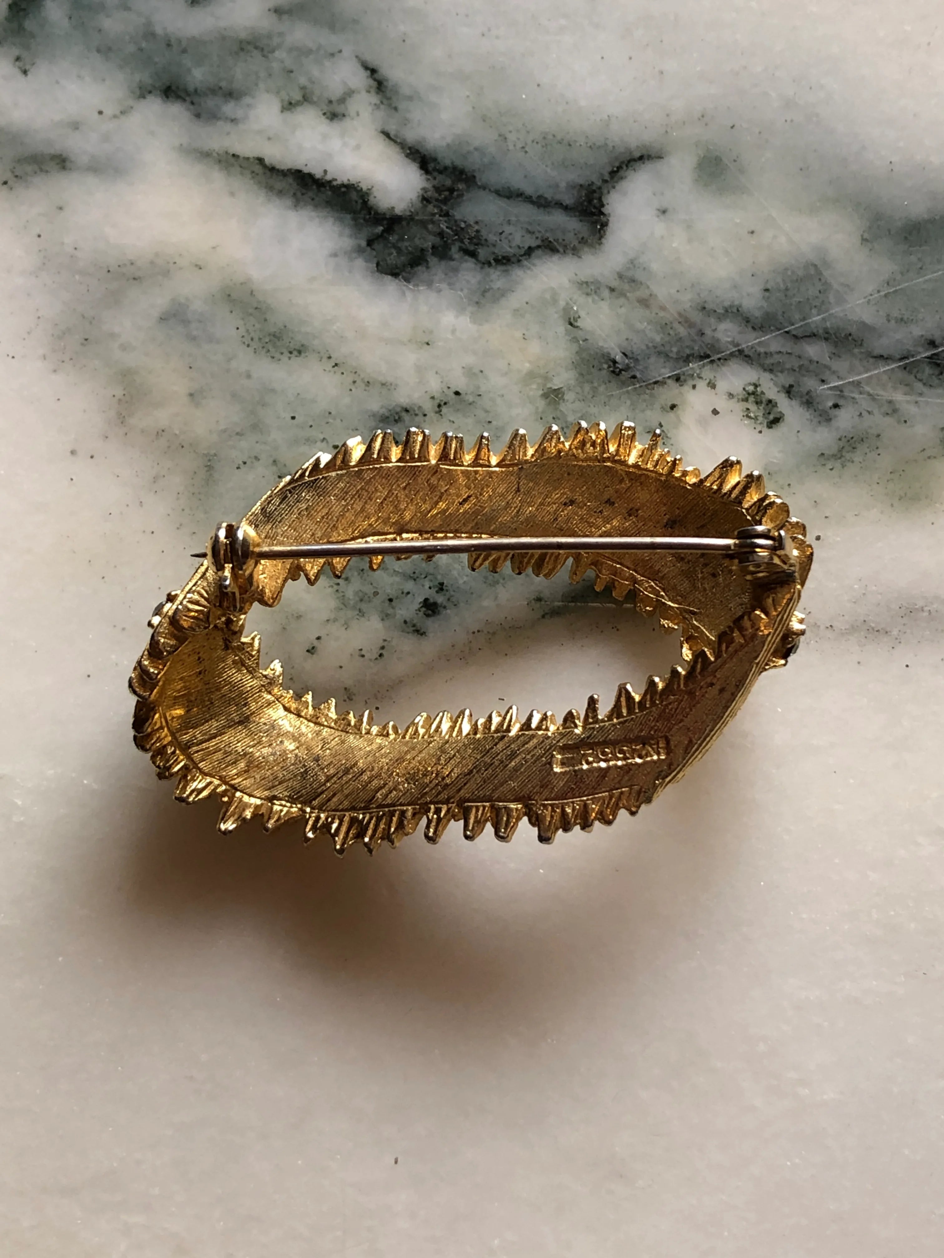 Broochella Anello di Luce vintage gold-tone oval brooch with textured overlapping forms and clear crystal accents. The background is white marble.