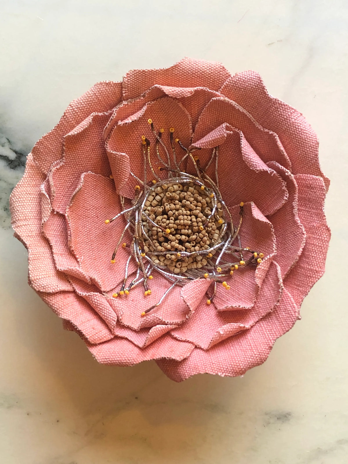 Broochella Anemone Flower Brooch Pin in soft denim pink, featuring sculptural layered fabric petals with a hand-beaded centre and delicate metallic stamen detailing on a cream marble background.