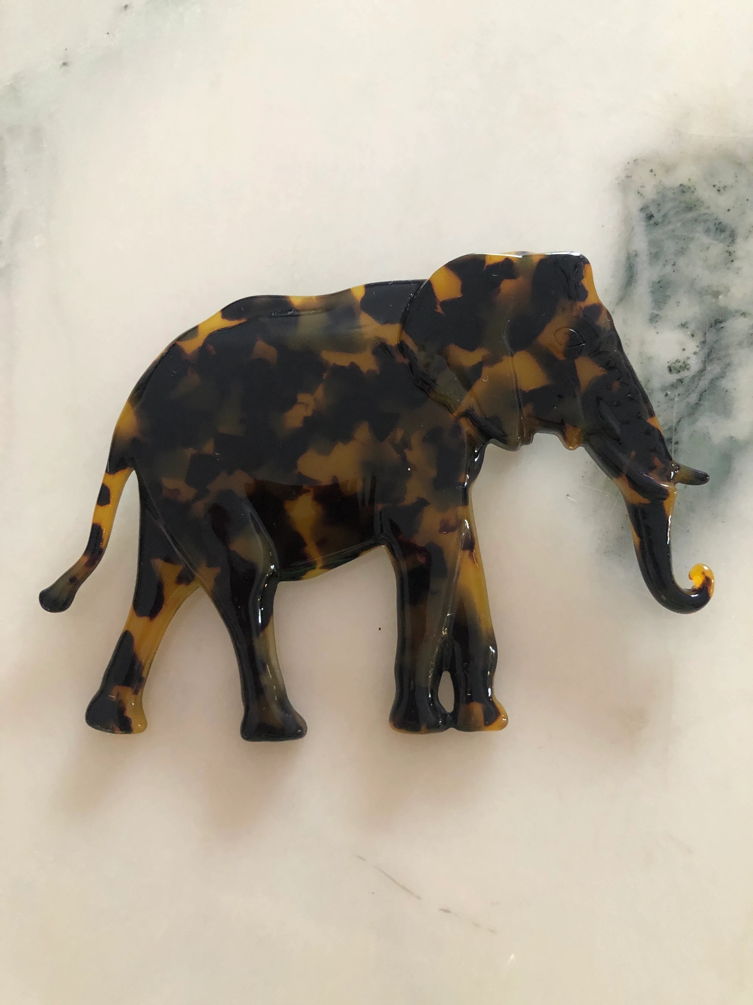 Broochella Animalia brown, figural  hand crafted, cellulose acetate elephant brooch in brown tortoiseshell. The background is white marble.