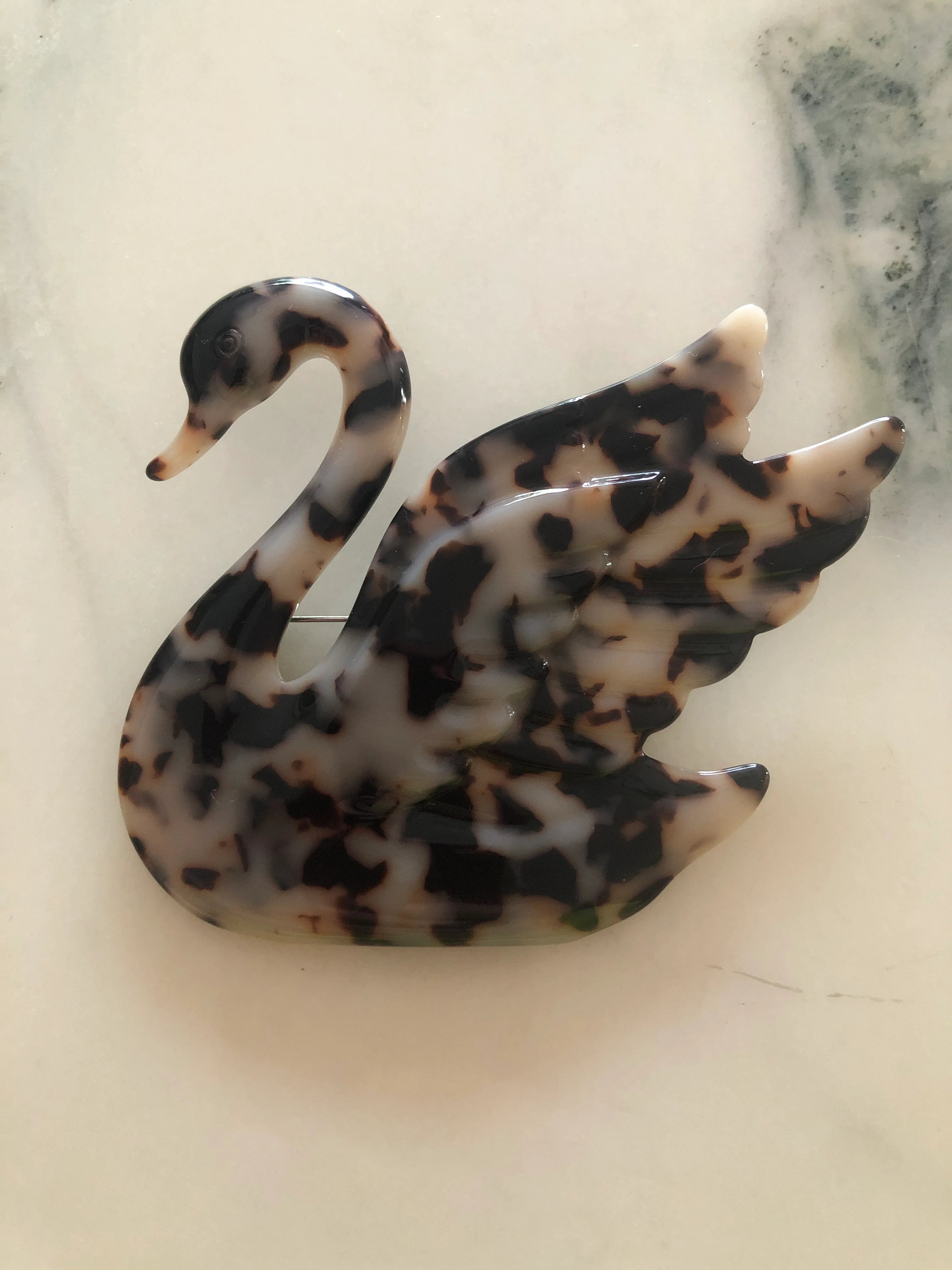 Broochella Animalia  Beige Tortoiseshell-patterned, hand made, designer swan-shaped brooch on a marble surface