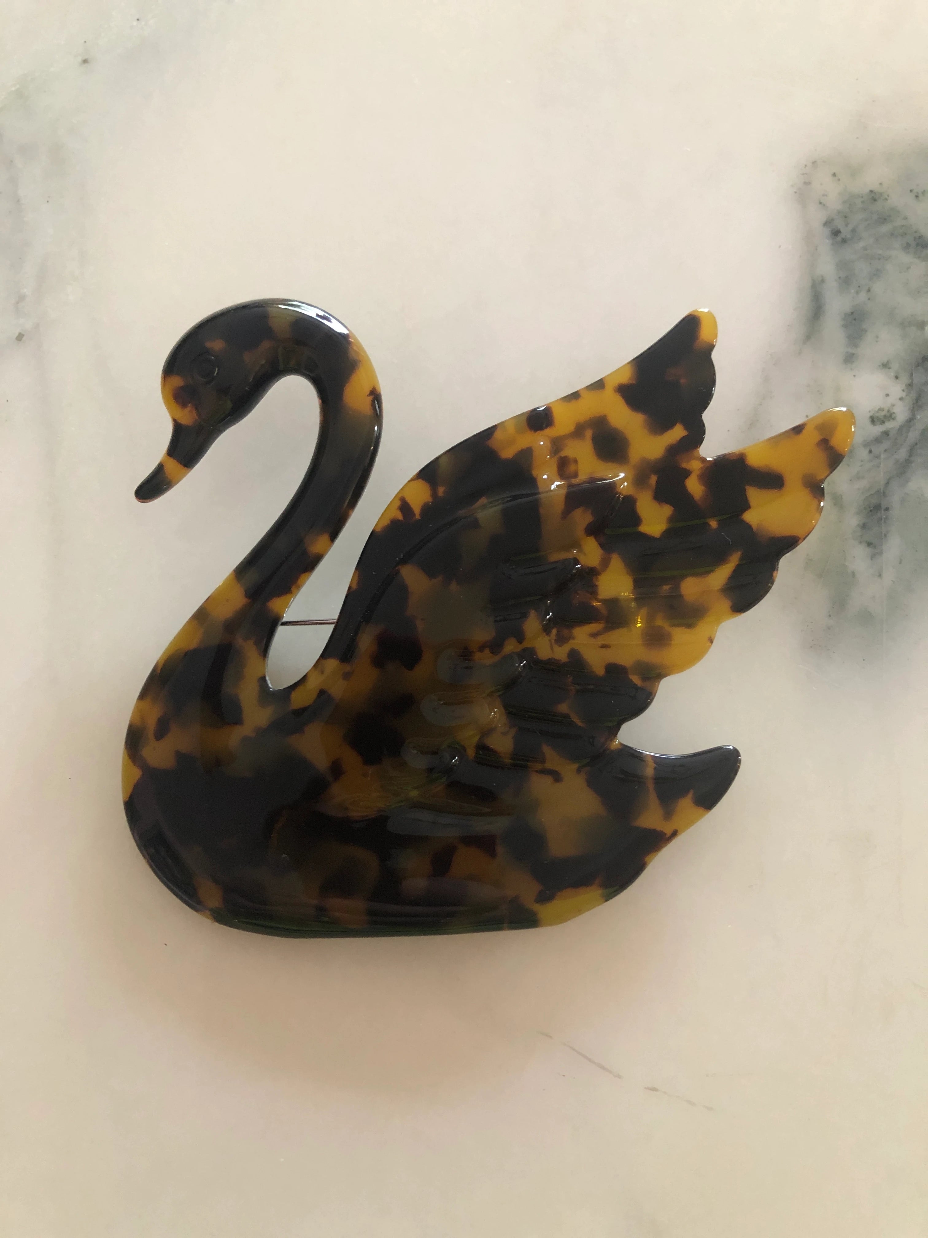 Broochella Animalia  Beige Tortoiseshell-patterned, hand made, designer swan-shaped brooch on a marble surface