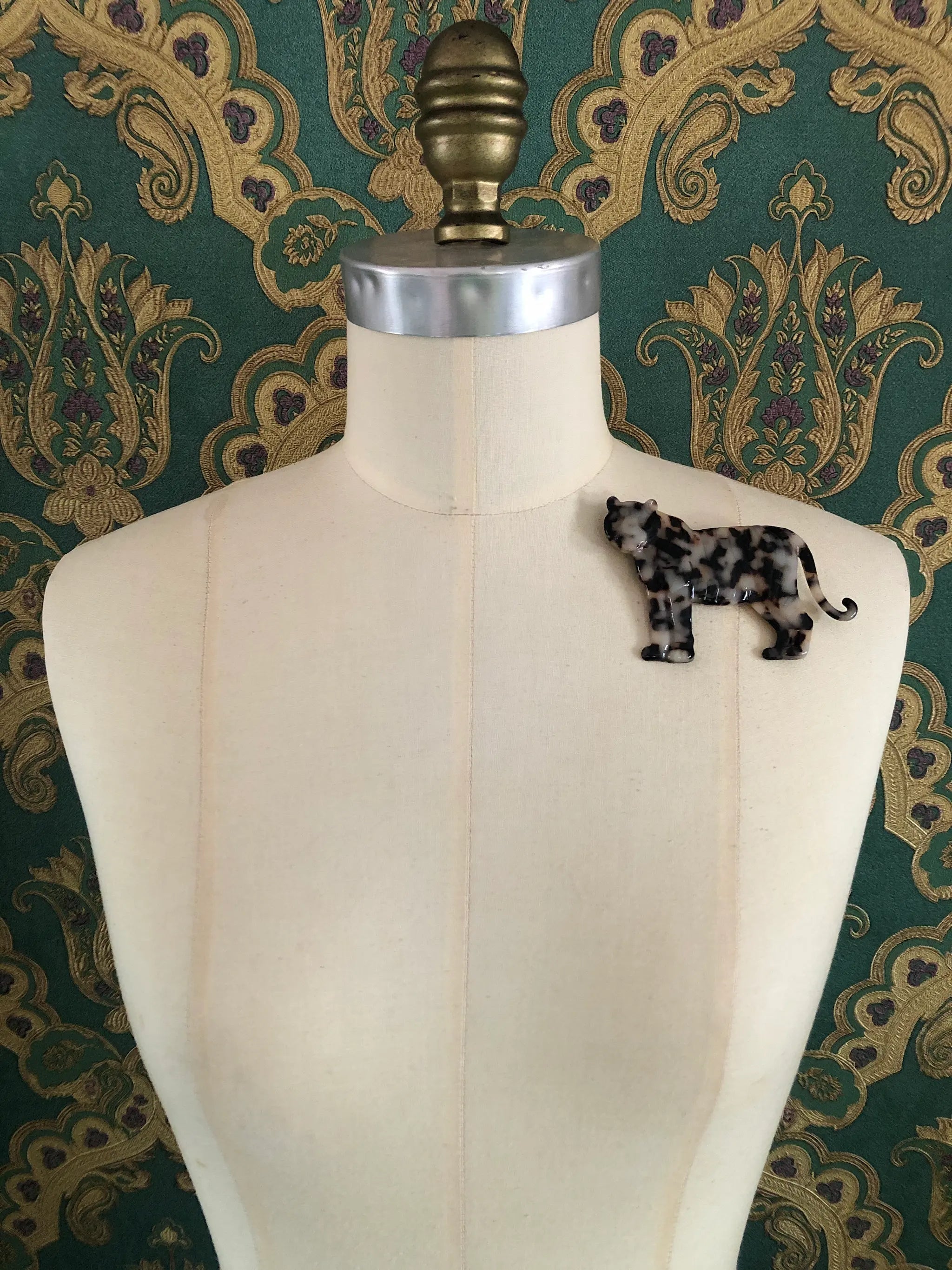 Broochella Animalia handmade tortoiseshell tiger brooch in Italian brown cellulose acetate. It is pinned to a mannequin. The background is green and gold damask wallpaper.