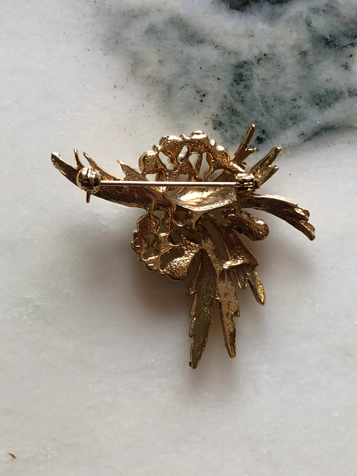 Broochella Antonella Vintage Pearl Leaf Brooch featuring clusters of ivory faux pearls amongst sculptural textured gold-tone leaves on a cream and grey marble background.