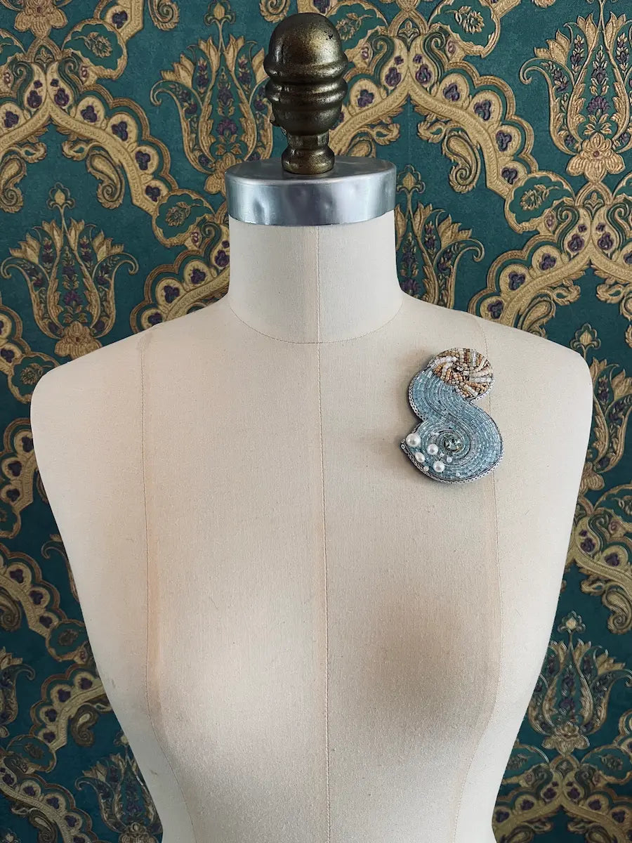 Broochella Aquarius hand beaded designer brooch. The background is green and gold damask wallpaper