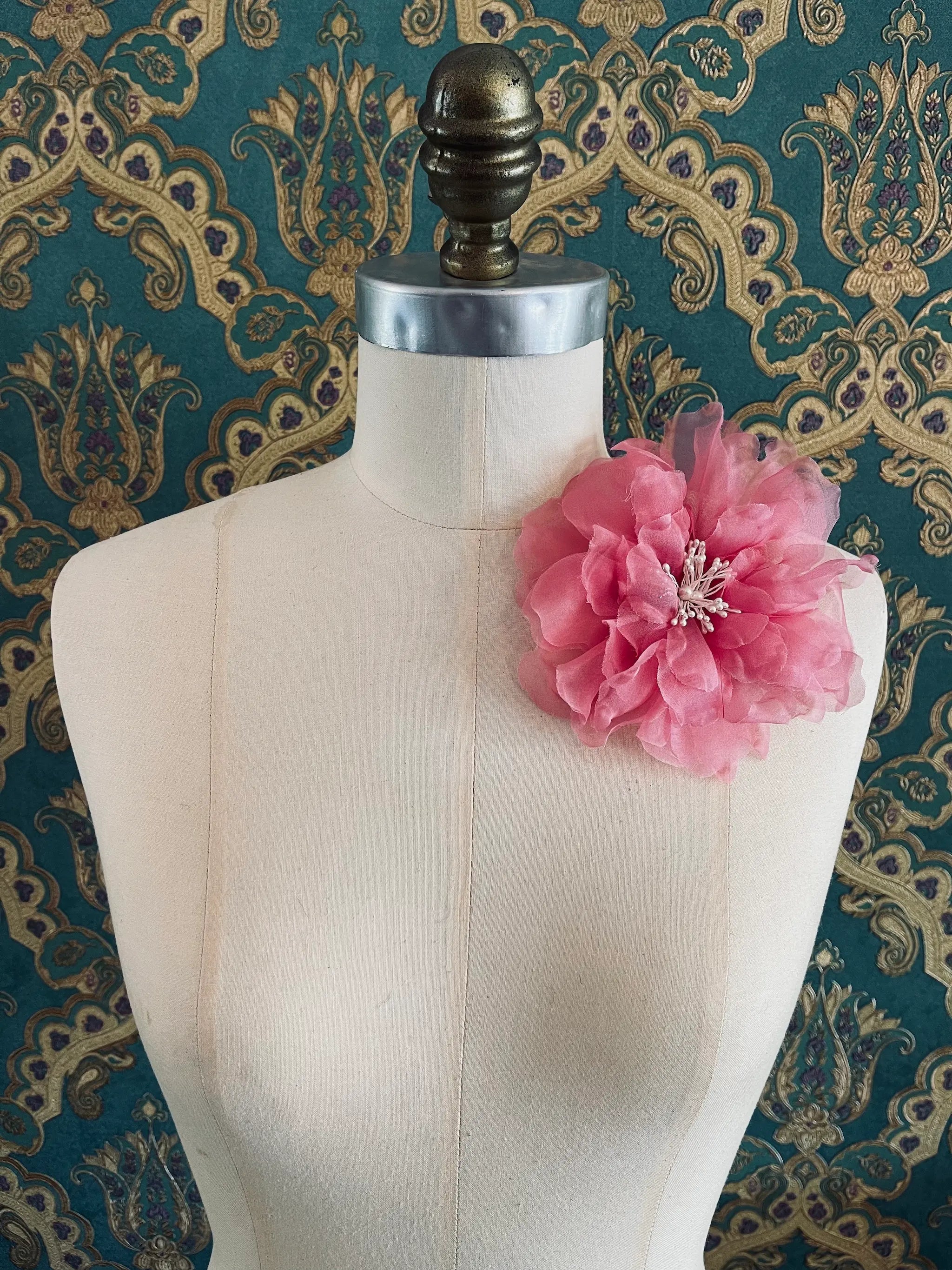Broochella Aubrieta handmade fabric flower brooch in blush pink. Pictured on a mannequin. The background is green and gold damask wallpaper