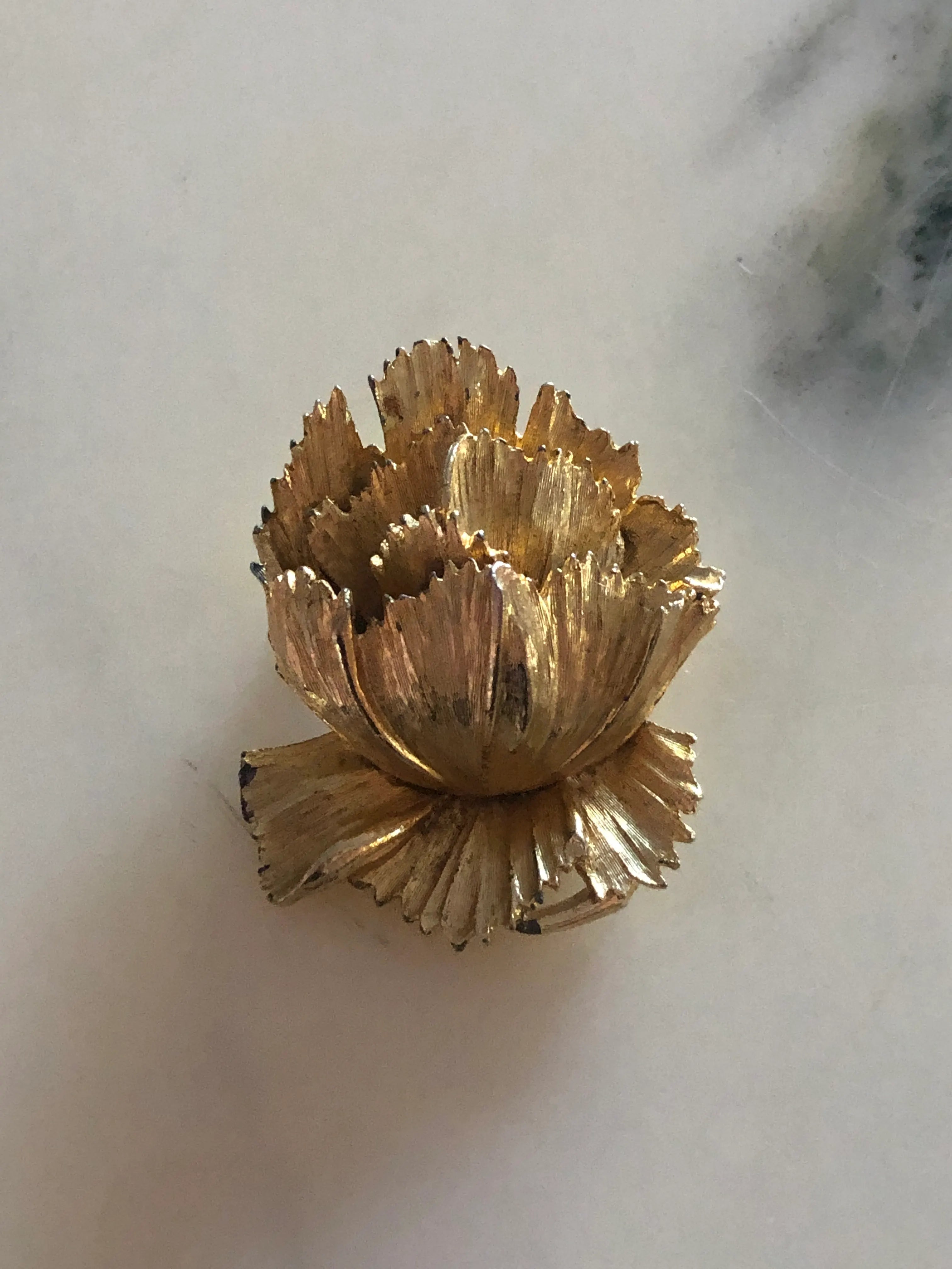 Broochella Aureo vintage gold tone metal flower brooch. The background is white marble. 