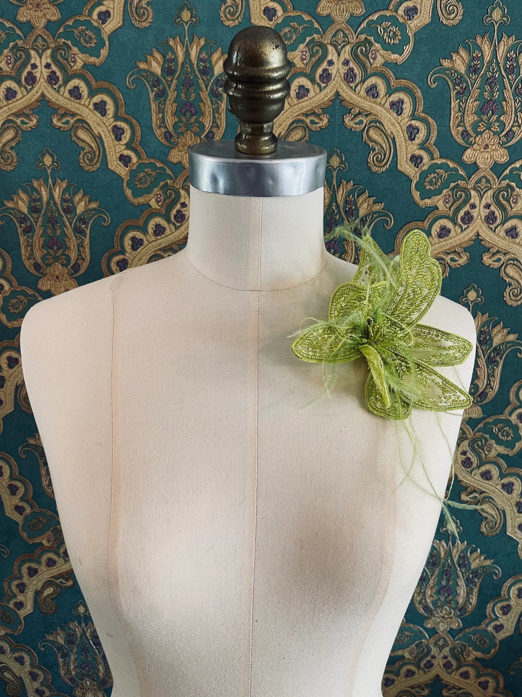 Broochella Azalea hand beaded flower brooch in chartreuse. Pictured on a mannequin. The background is green and gold damask wallpaper