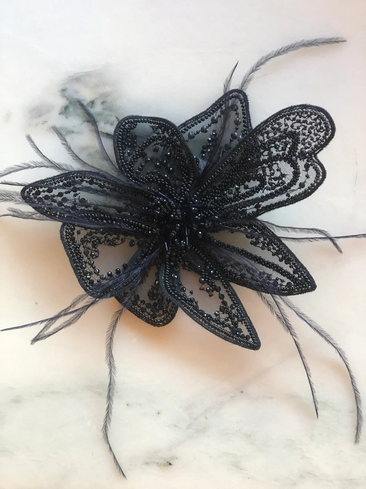 Broochella Azalea Flower Hand-Beaded Bridal Brooch in black, small size, featuring layered sheer petals embellished with intricate black beading, sequins and delicate feathers, photographed on a white marble background with subtle grey veining.