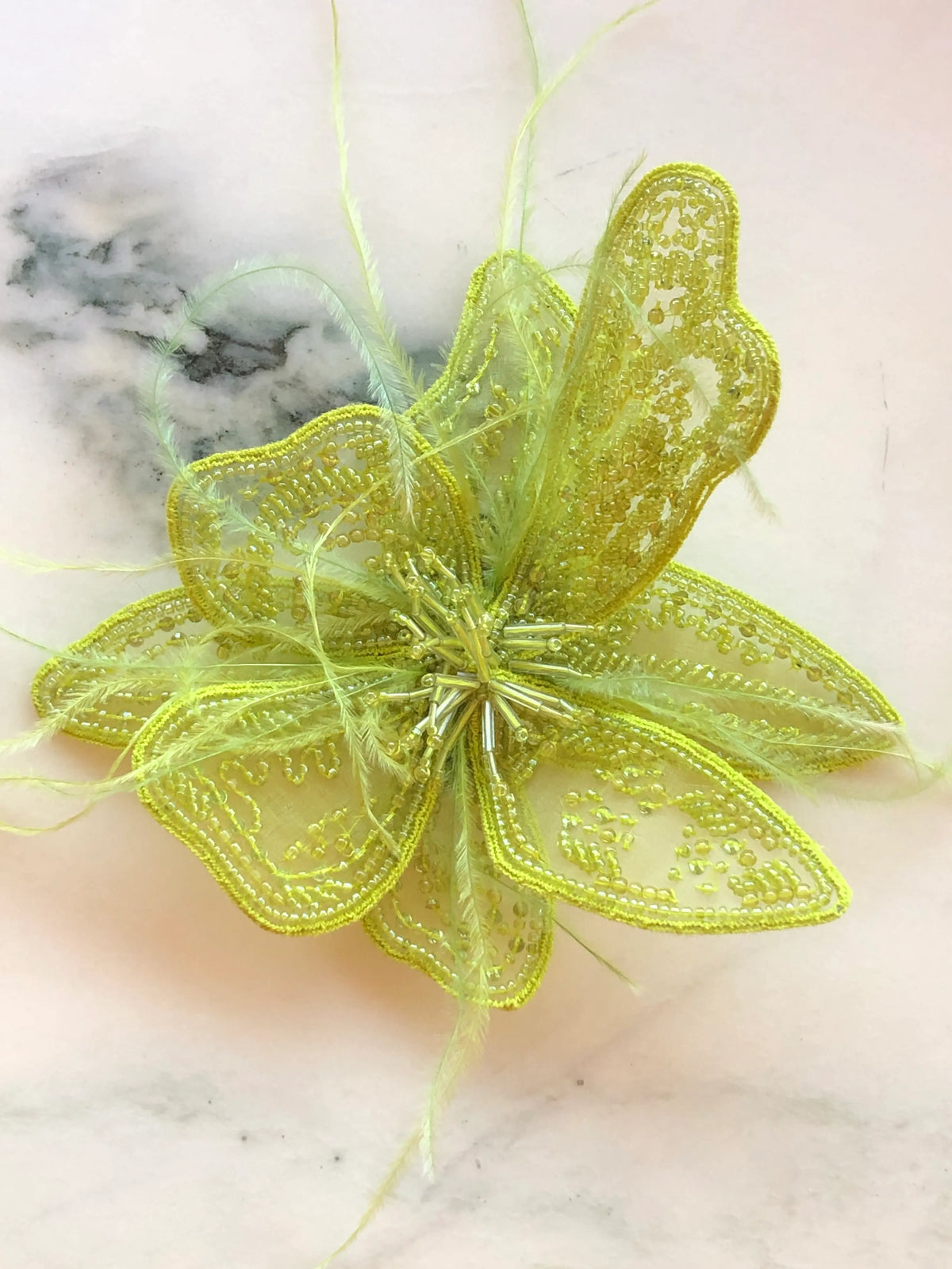 Broochella Men's Azalea Flower Hand-Beaded Brooch Pin - Small in chartreuse, featuring intricate chartreuse beadwork on sheer sculptural petals with delicate tonal feather accents on a cream marble background.