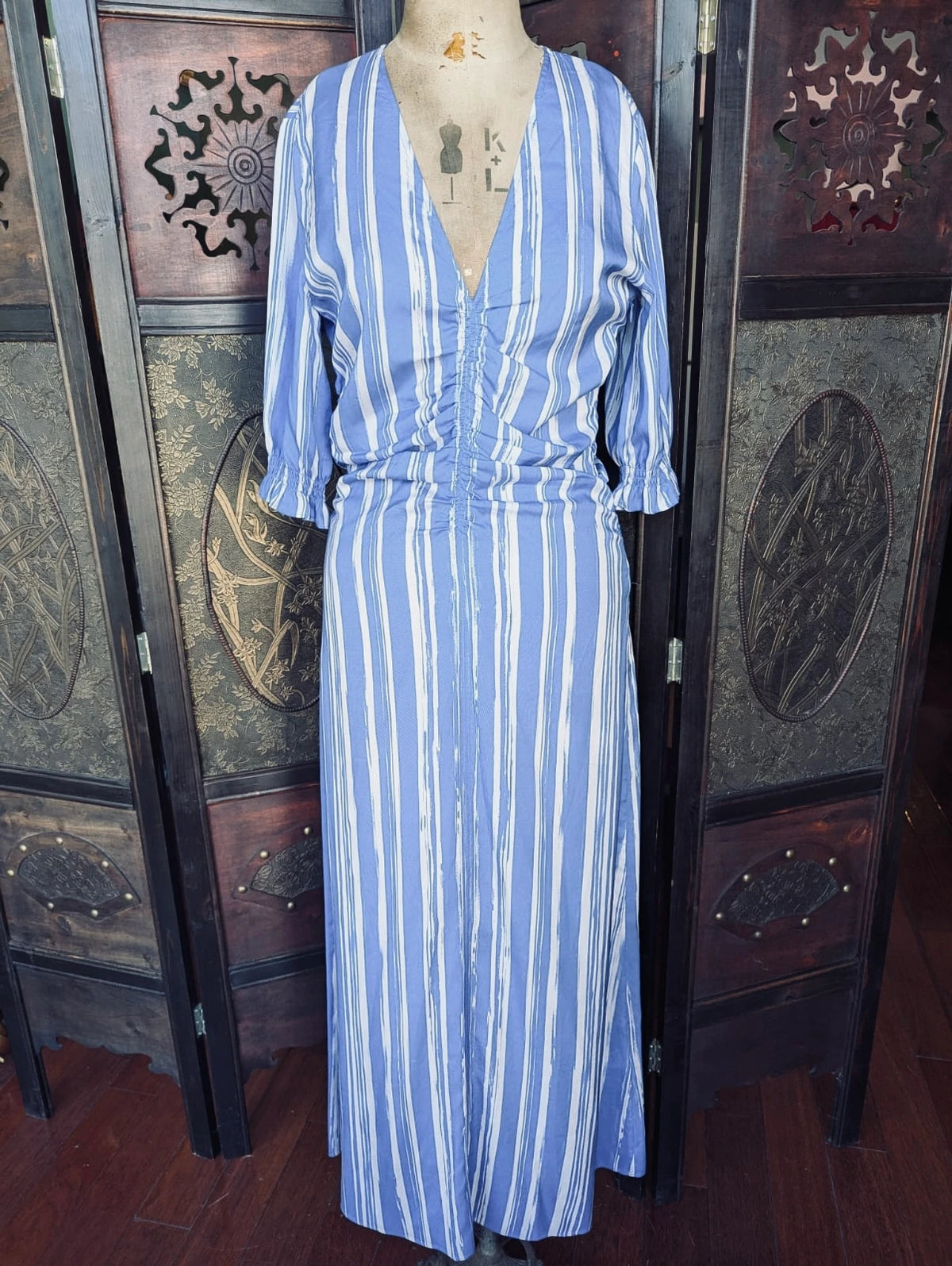 Broochella Baum und Pferdgarten Silk Maxi – Size 38 Blue and white striped dress on a mannequin against a decorative wooden screen.