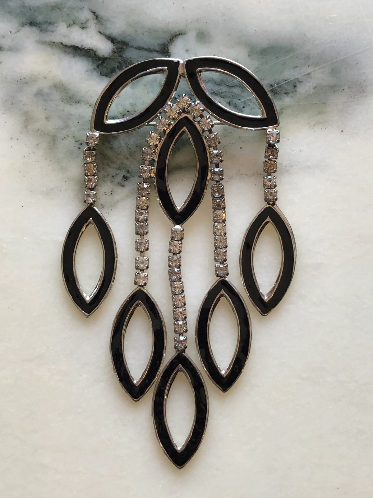 Broochella Beatrice Vintage Black Enamel Cascade Brooch featuring geometric black enamel shapes and cascading clear crystal strands in a silver-tone setting on a cream and grey marble background.