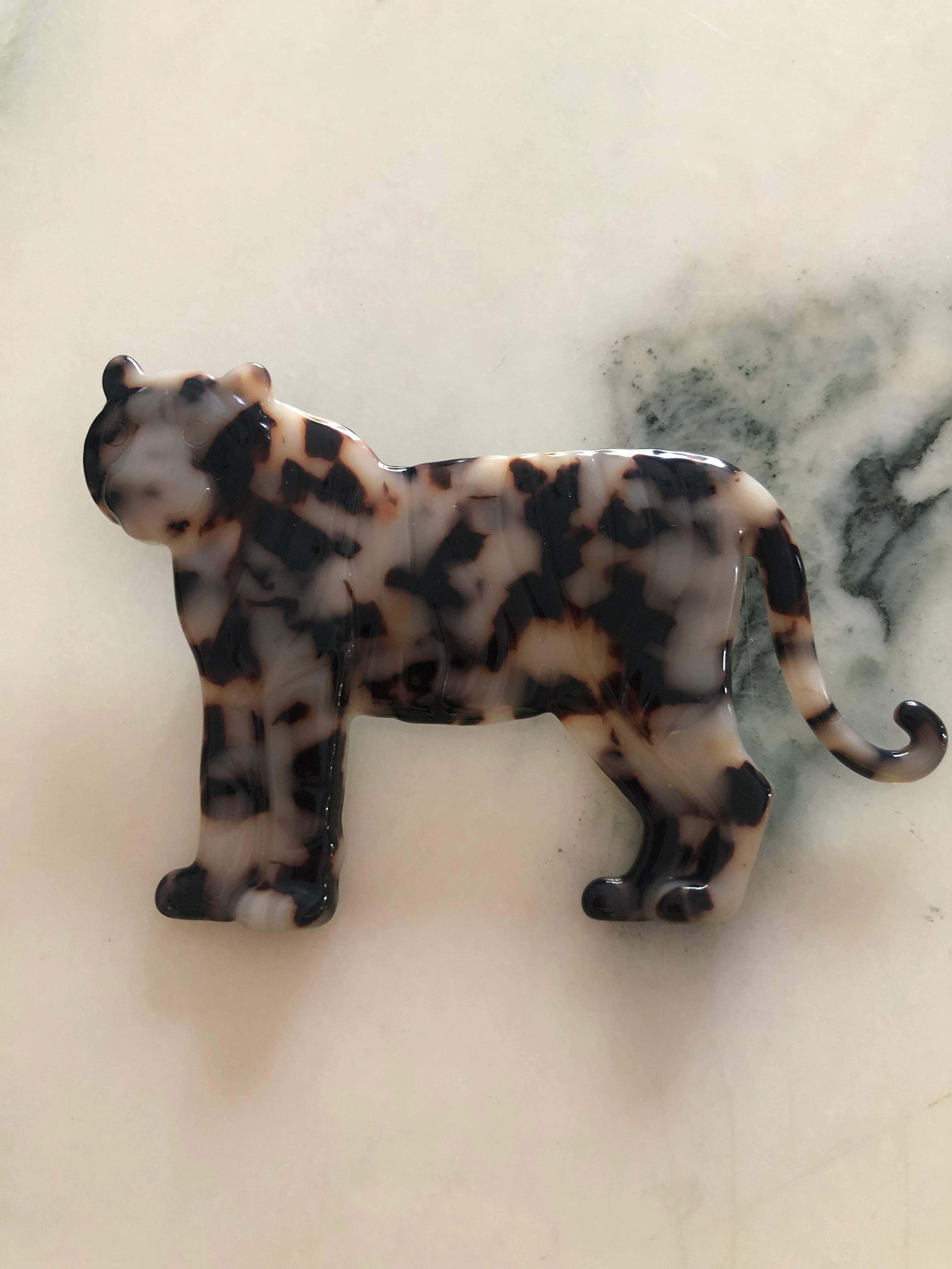 Broochella Men's beige Animalia tortoiseshell tiger shaped brooch. It is made from Premium Italian cellulose tortoiseshell acetate. It is presented on a white marble surface. 