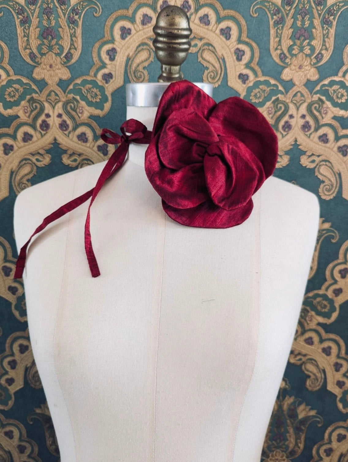 Broochella Bellucci large burgundyhandmade silk flower brooch and choker  Pictured on a mannequin. The background is green and gold damask wallpaper.