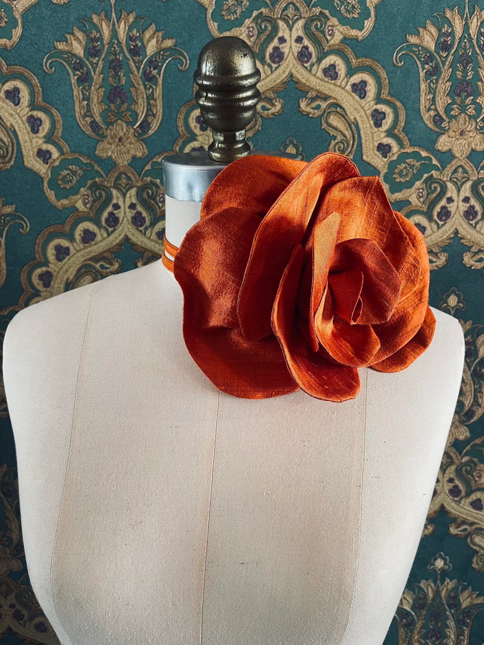 Broochella Bellucci large orange handmade silk flower brooch and choker  Pictured on a mannequin. The background is green and gold damask wallpaper.