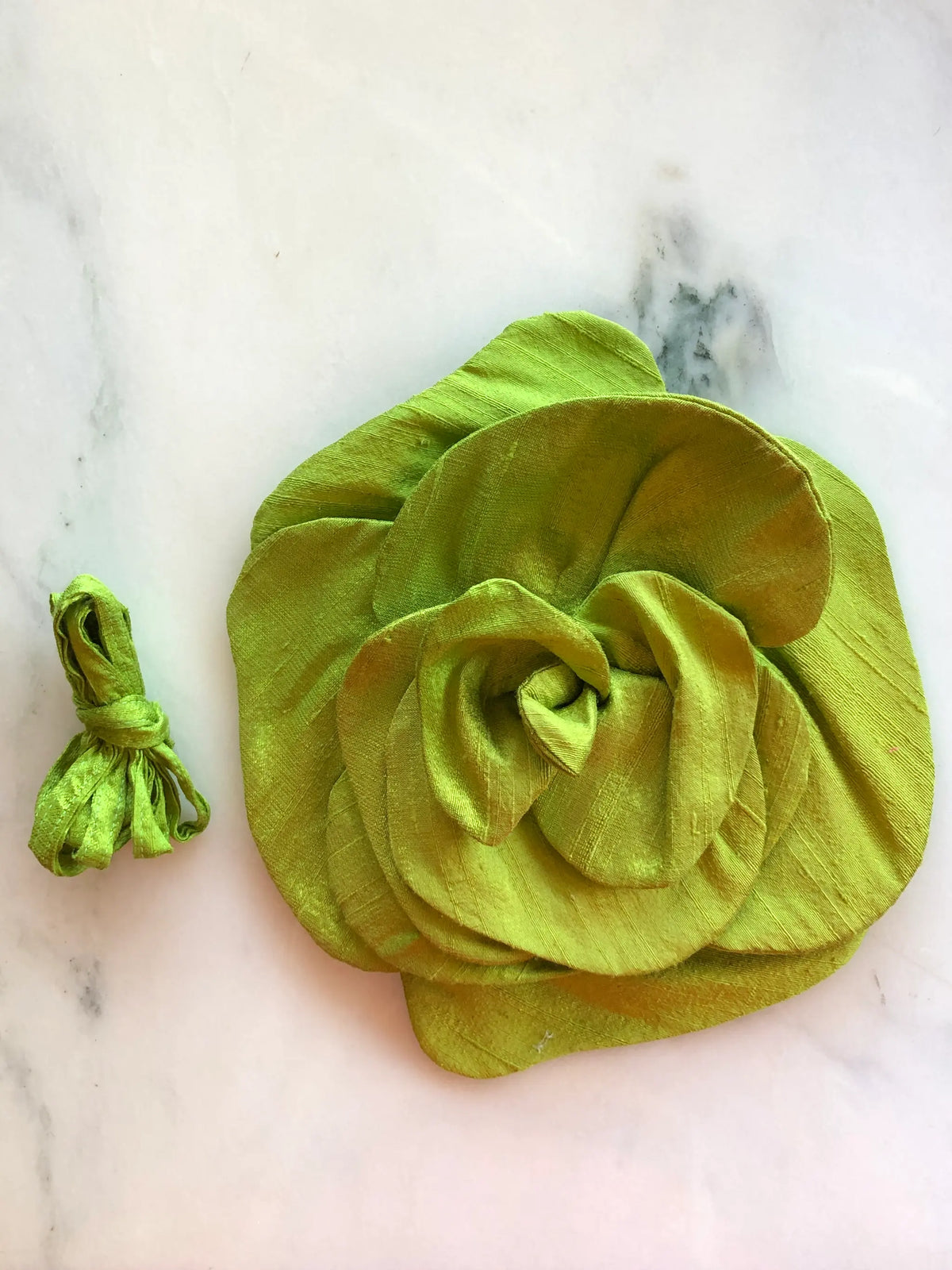 Broochella Bellucci Large Silk Flower Brooch & Choker in chartreuse green, with sculptural layered silk petals and matching ribbon, photographed on a white marble background with soft grey veining.