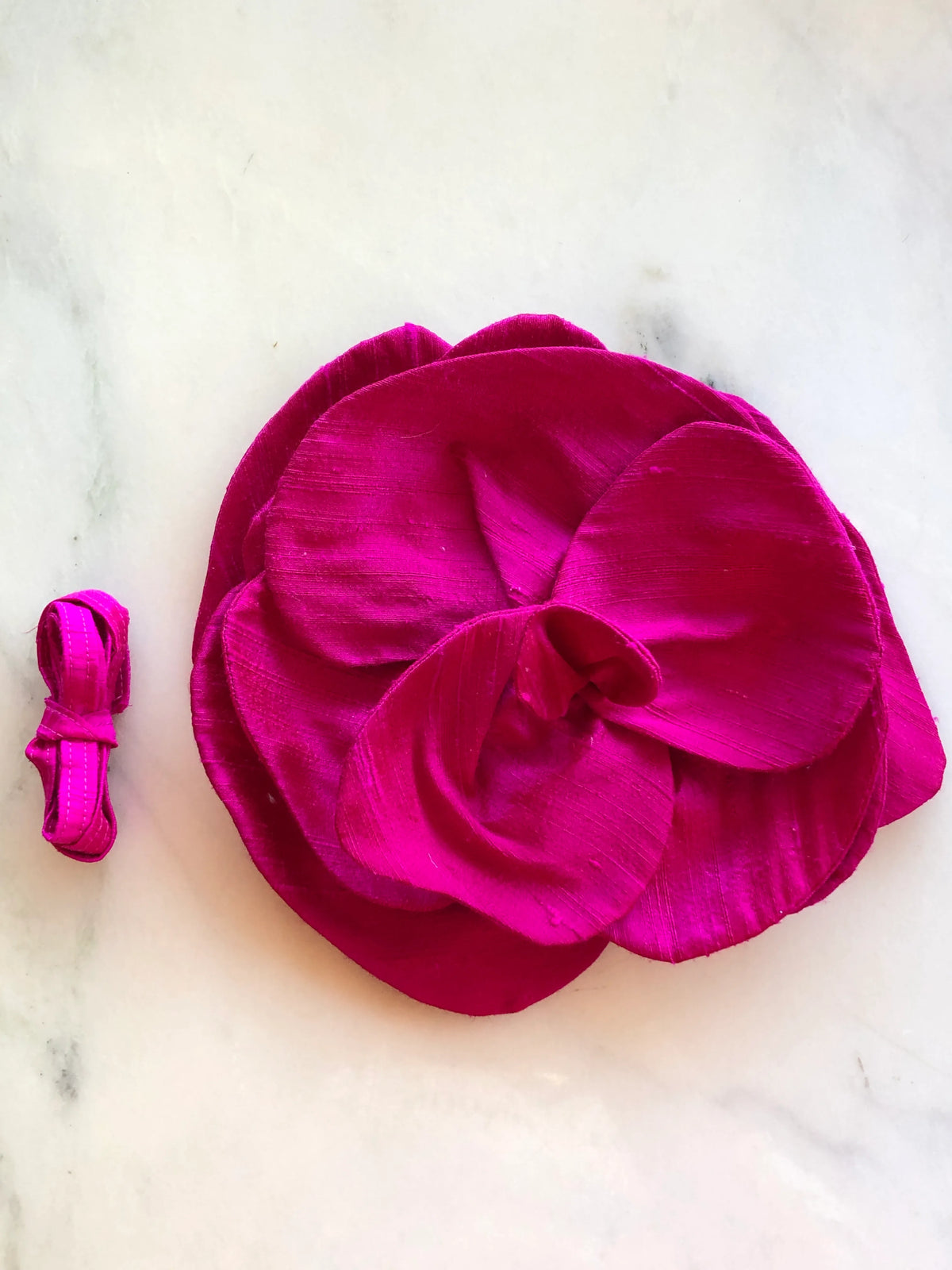 Broochella Bellucci Large Silk Flower Brooch & Choker in vibrant pink, with sculptural layered silk petals and matching ribbon, photographed on a white marble background with subtle grey veining.