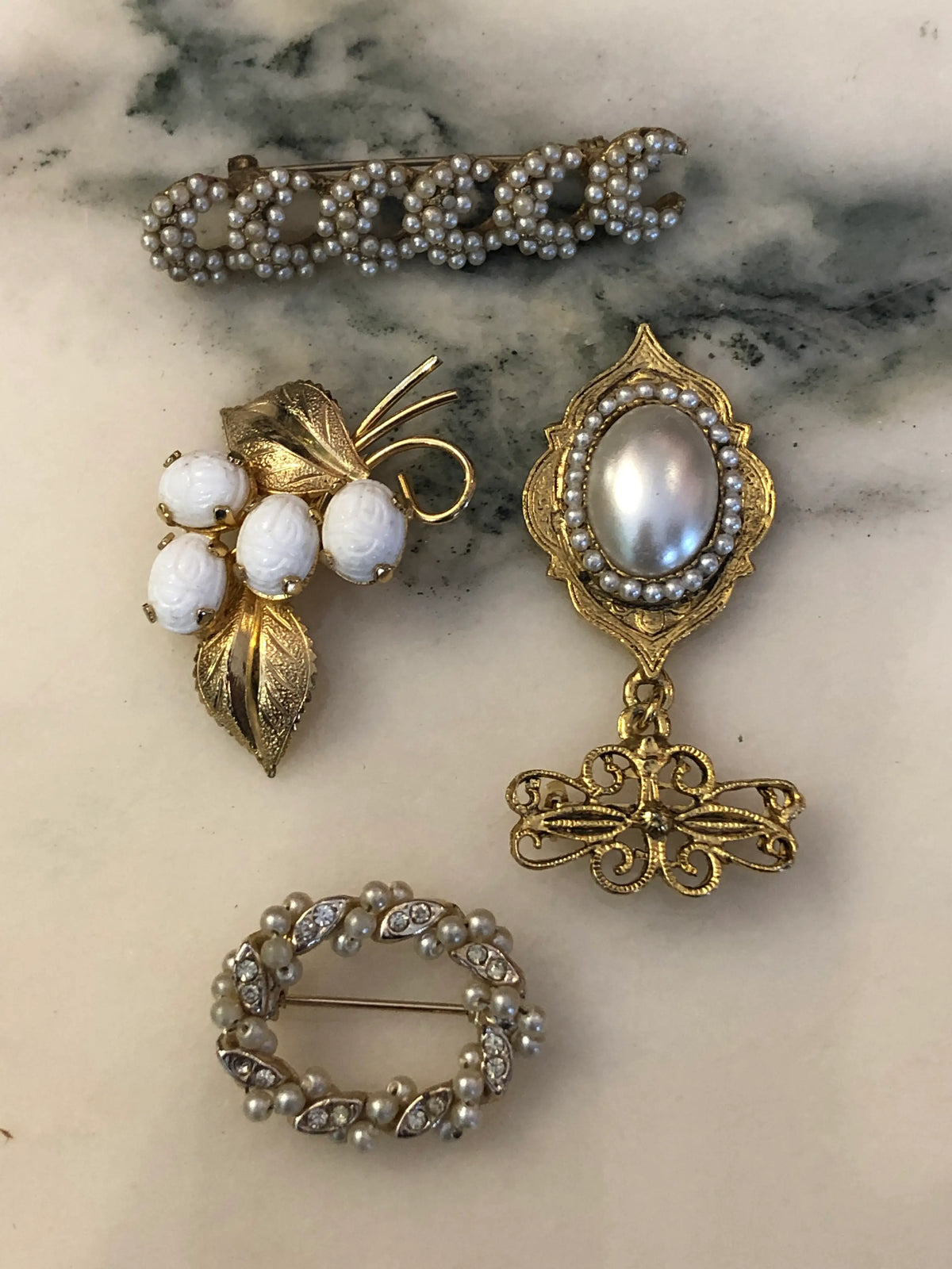 Broochella The Bianca Vintage Brooch Quartet featuring four ornate vintage pearl, ivory and gold-tone brooches with botanical, scroll and filigree details on a cream and grey marble background.