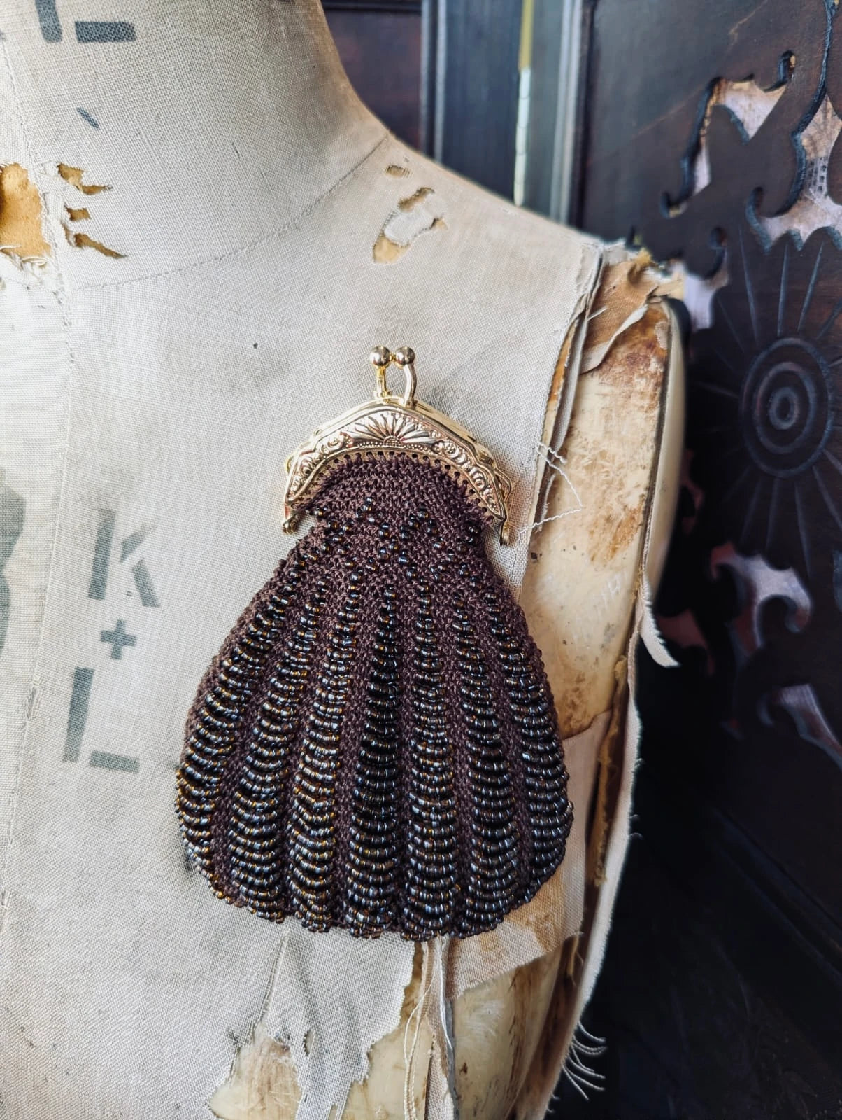 Broochella Borsellino vintage brown beaded purse brooch with gold clasp. It is pinned to a vintage mannequin. The background is a decorative dark wood screen.