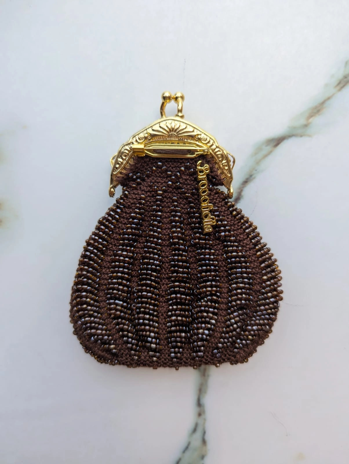 Broochella Borsellino vintage brown beaded purse brooch with gold clasp. It is pinned to a vintage mannequin. The background is a white marble.