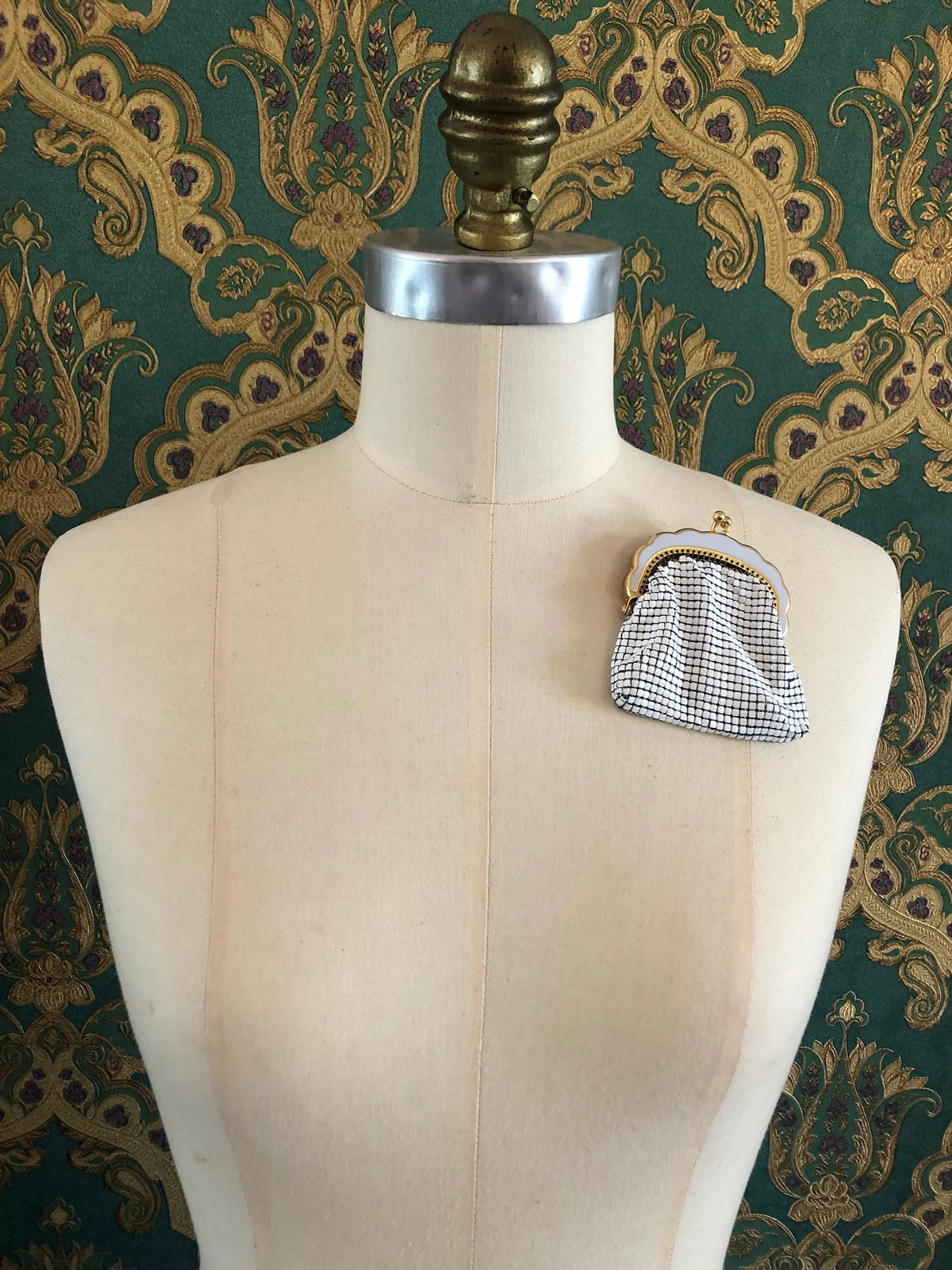 Broochella Borsellino vintage purse brooch pin in white mesh with a gold-tone frame, displayed on a cream dress form against an ornate green and gold patterned brocade background.