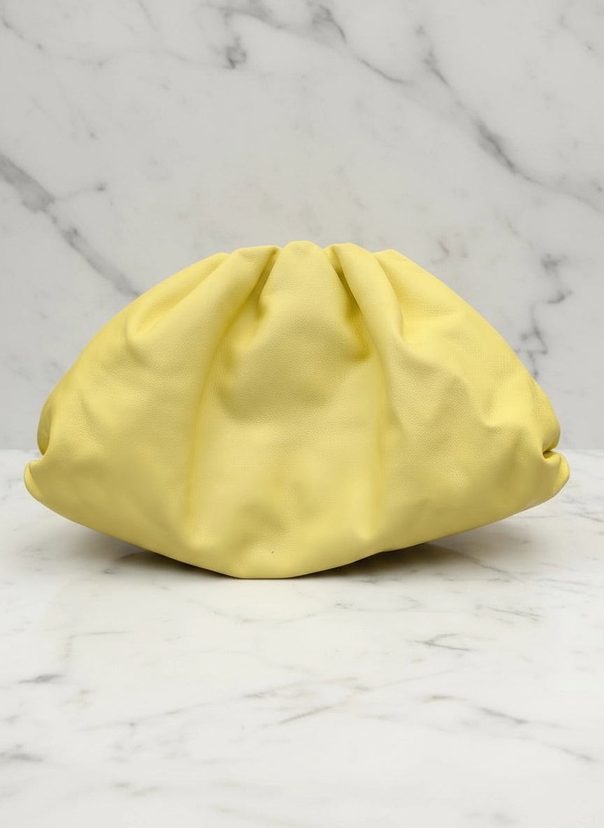 A Broochella Bottega Veneta The Pouch pale yellow large leather pouch clutch bag purse  with gathered pleats, placed on a white marble surface with gray veining.