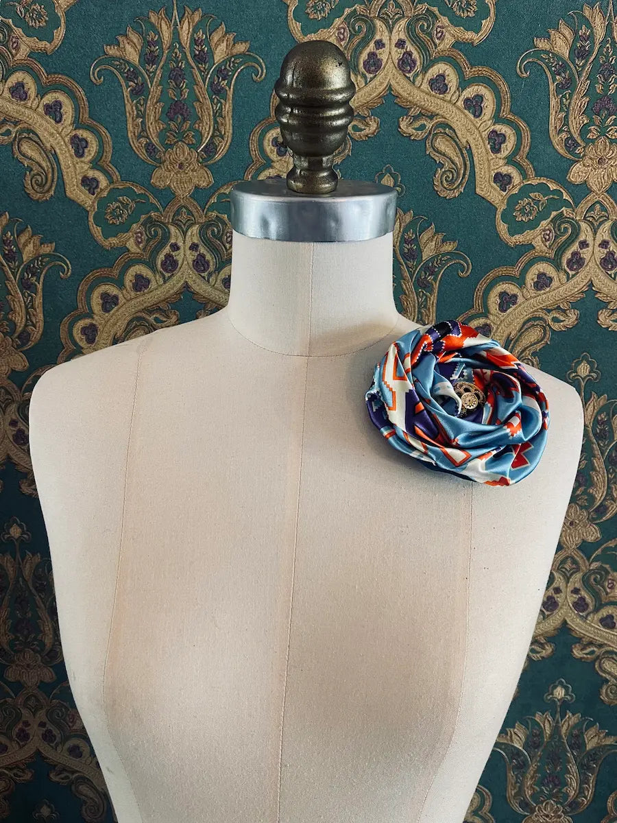 Broochella bougainville handmade blue designer satin flower brooch pictured on a mannequin the background is green and gold damask wallpaper