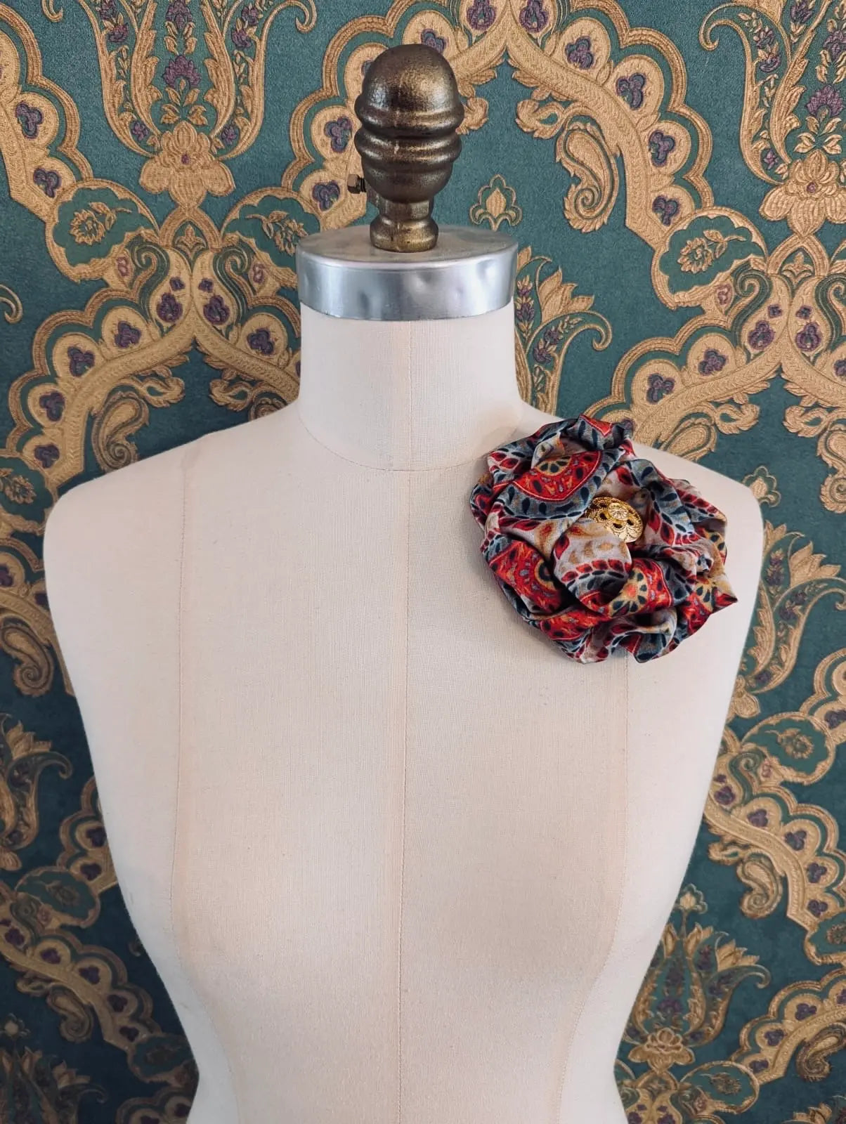 Broochella bougainville handmade red designer satin flower brooch pictured on a mannequin the background is green and gold damask wallpaper