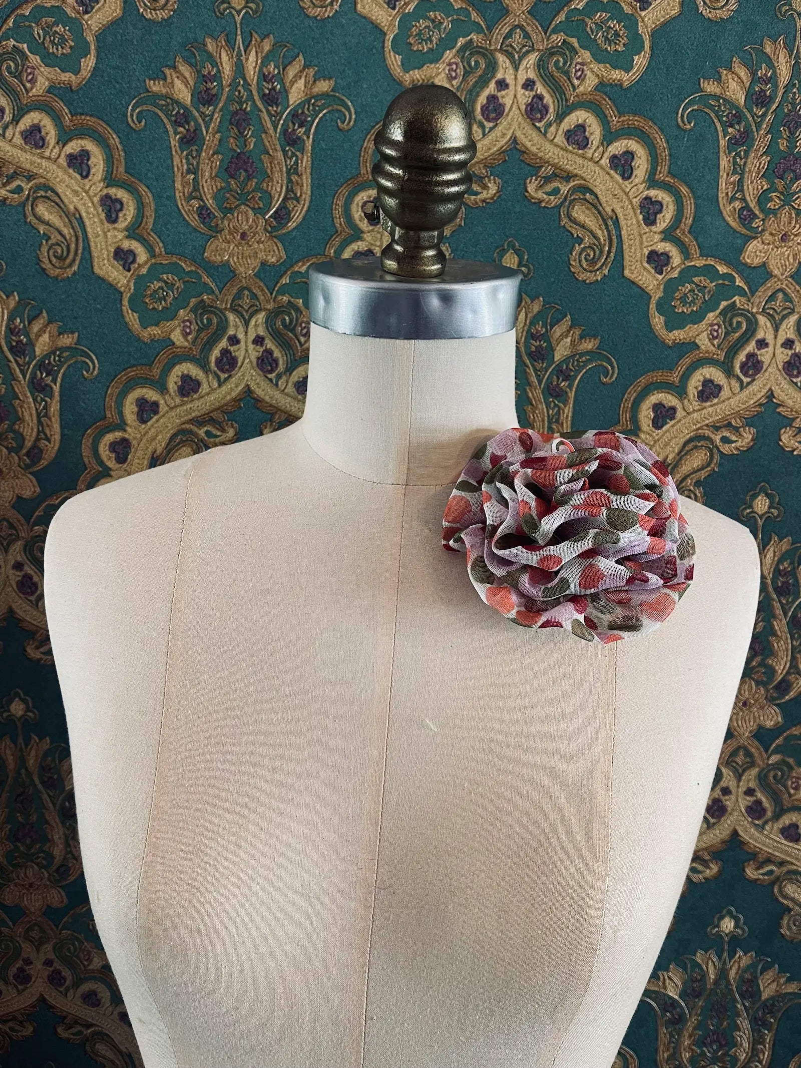 Broochella Brassica handmade fabric flower brooch in white with pink and green polka dots. Styled on a mannequin. The background is green and gold damask wallpaper
