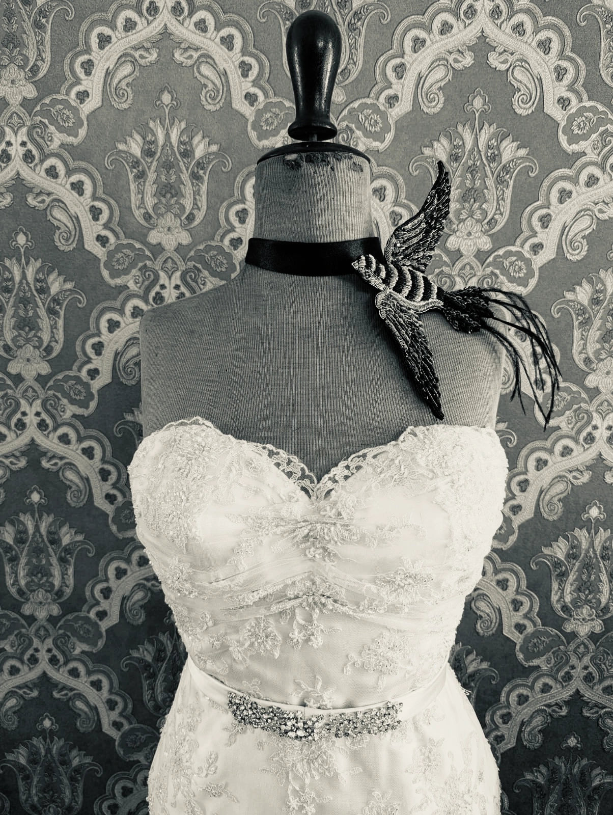 Broochella bridal  rondine swallow bird hand beaded pink and black brooch. Pictured on a mannequin that is wearing a white, beaded strapless wedding dress. The background is green and gold damask wallpaper. 