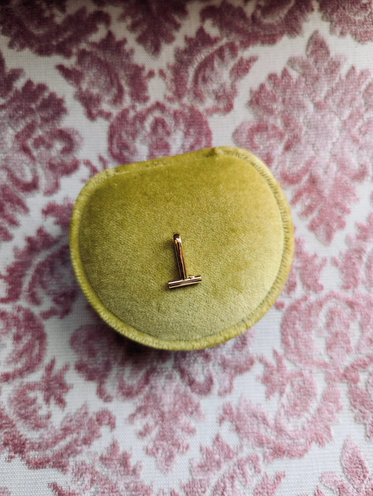 Broochella brooch to necklace converter in gold. it is sitting on a green velvet ring box. the background is pink damask fabric