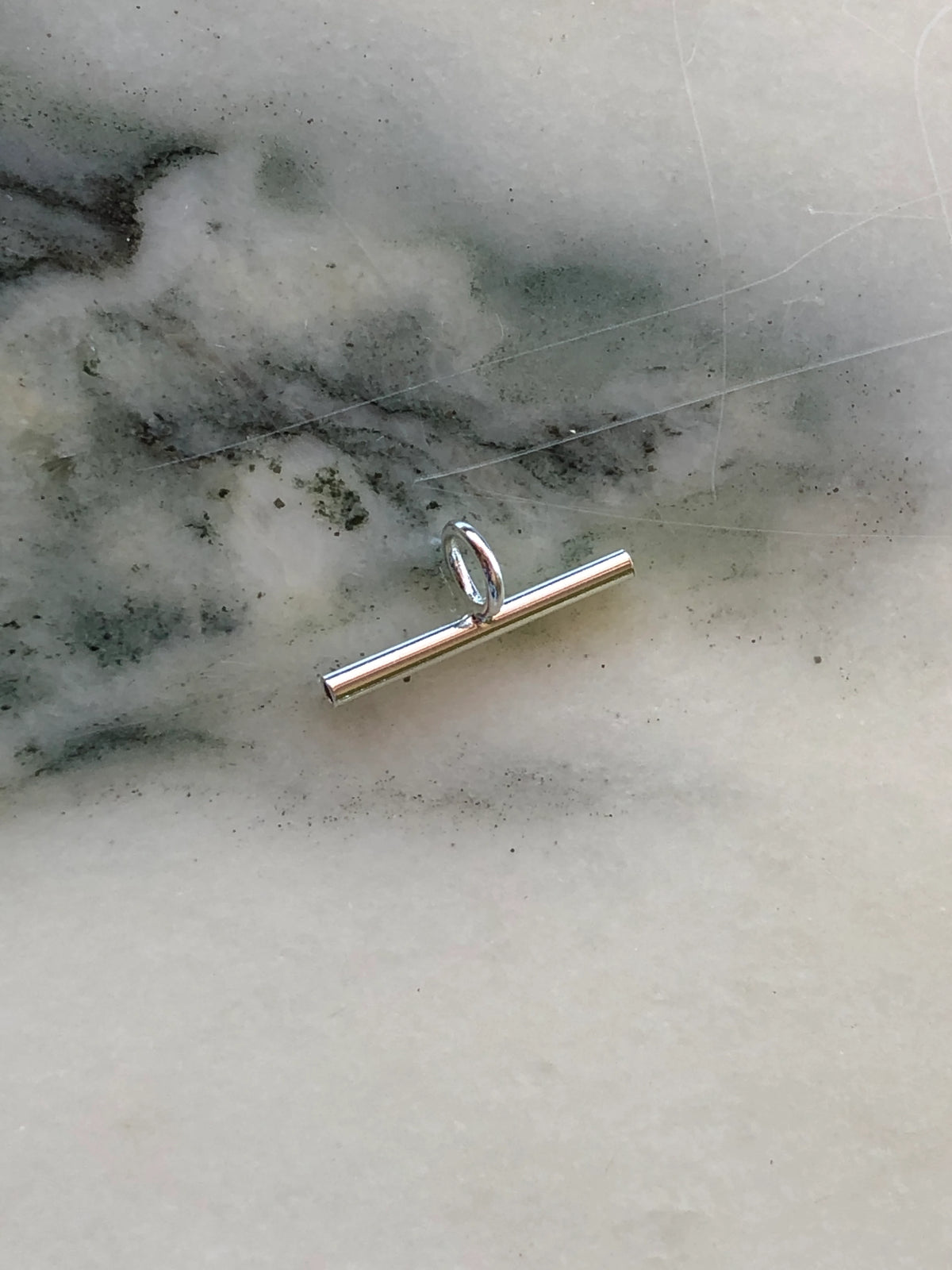 Broochella extended bar brooch to necklace converter in silver-tone metal with central oval loop, photographed on white marble with grey-green veining.