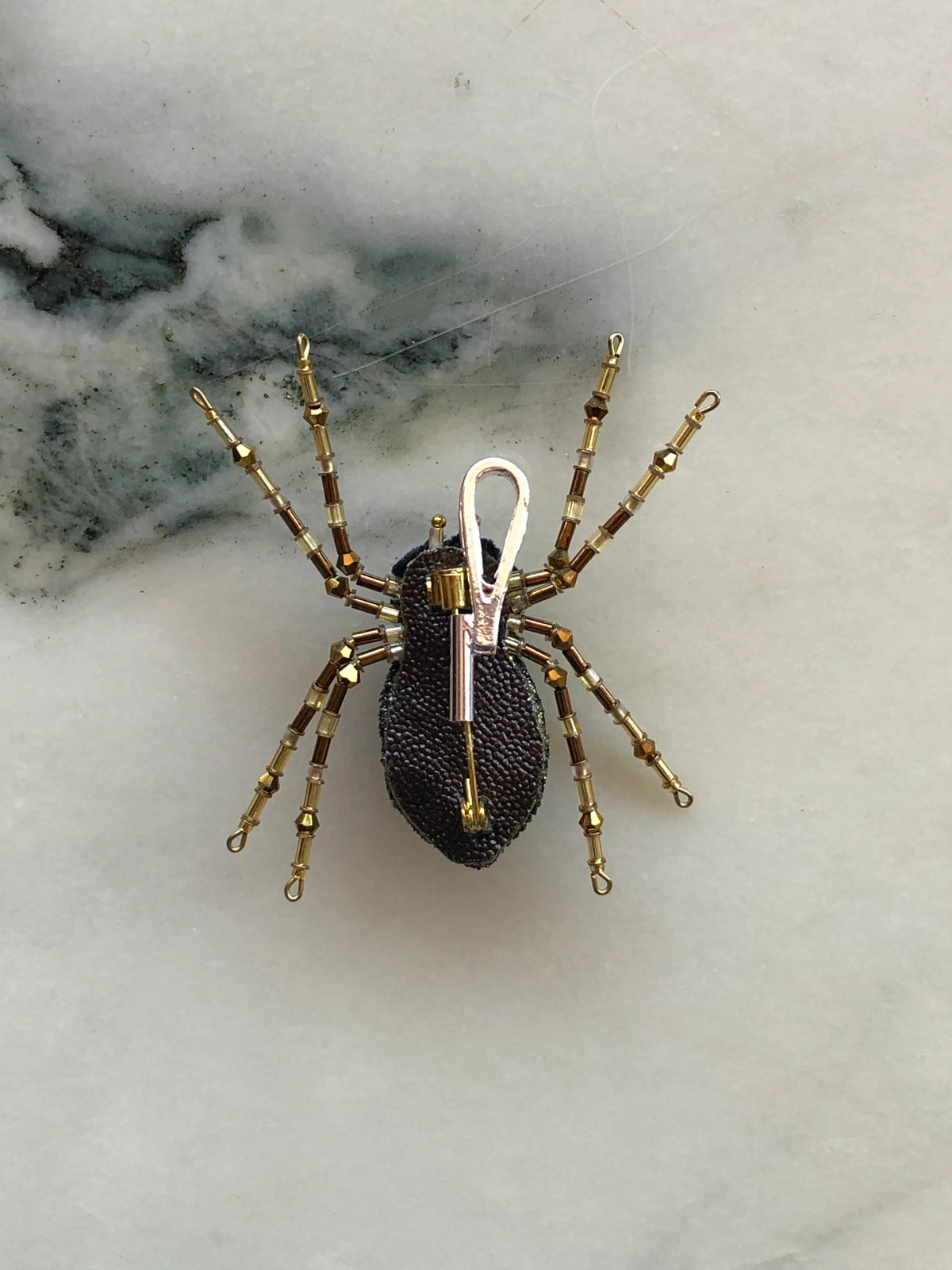 Broochella vertical brooch to necklace converter in silver-tone metal with elongated loop design. It is pictured in use on the Broochella spider brooch. It is photographed on white marble with grey-green veining.